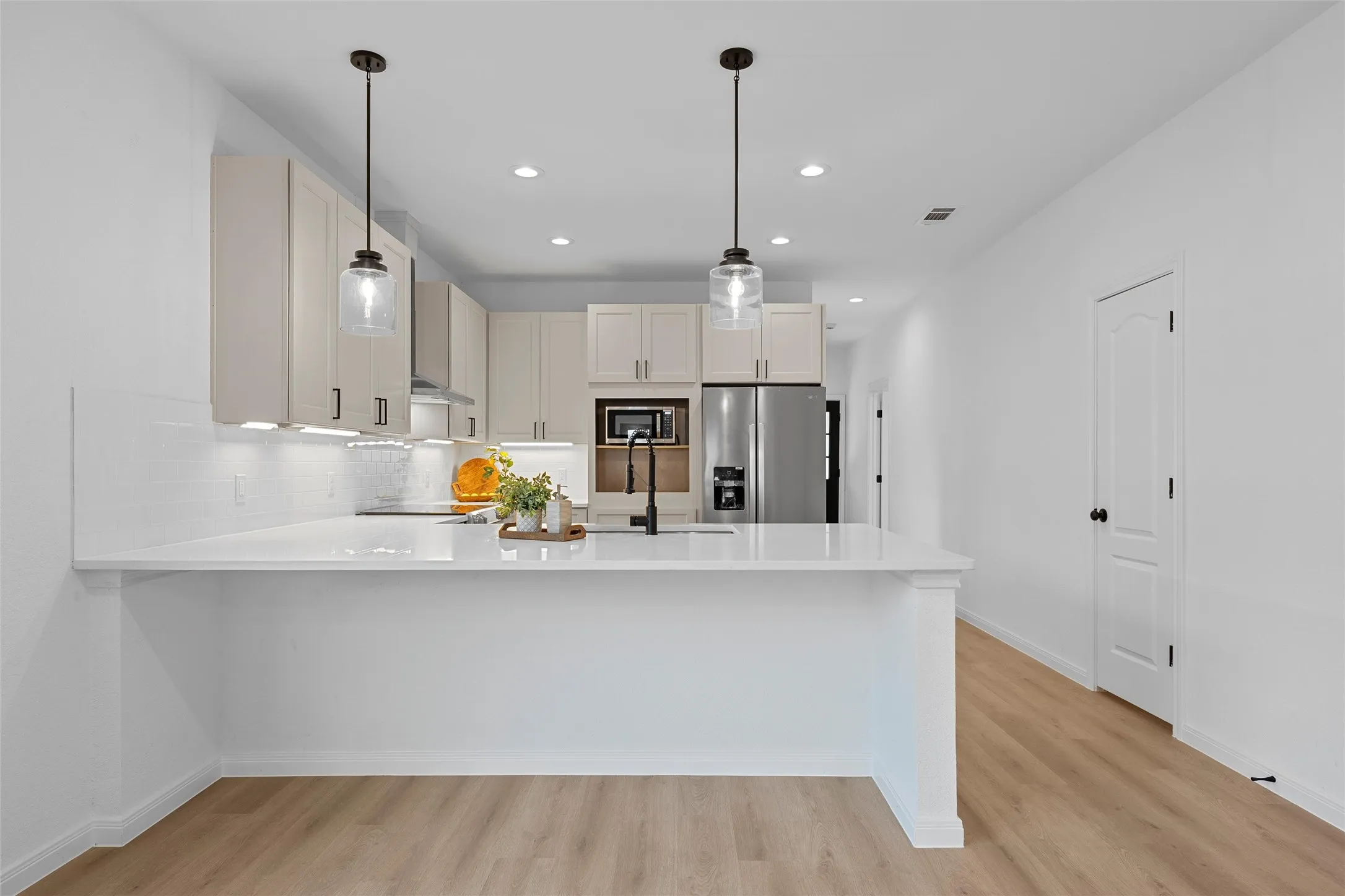 Kitchen with a peninsula, pendant lighting, stainless steel appliances, decorative backsplash, and light wood-style flooring