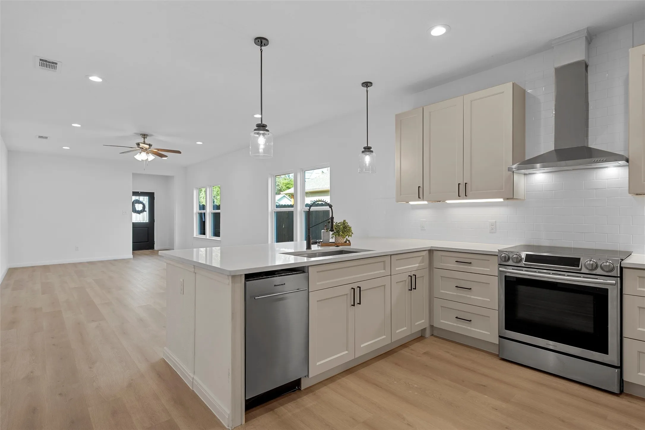 Kitchen with appliances with stainless steel finishes, range hood, backsplash, decorative light fixtures, and recessed lighting
