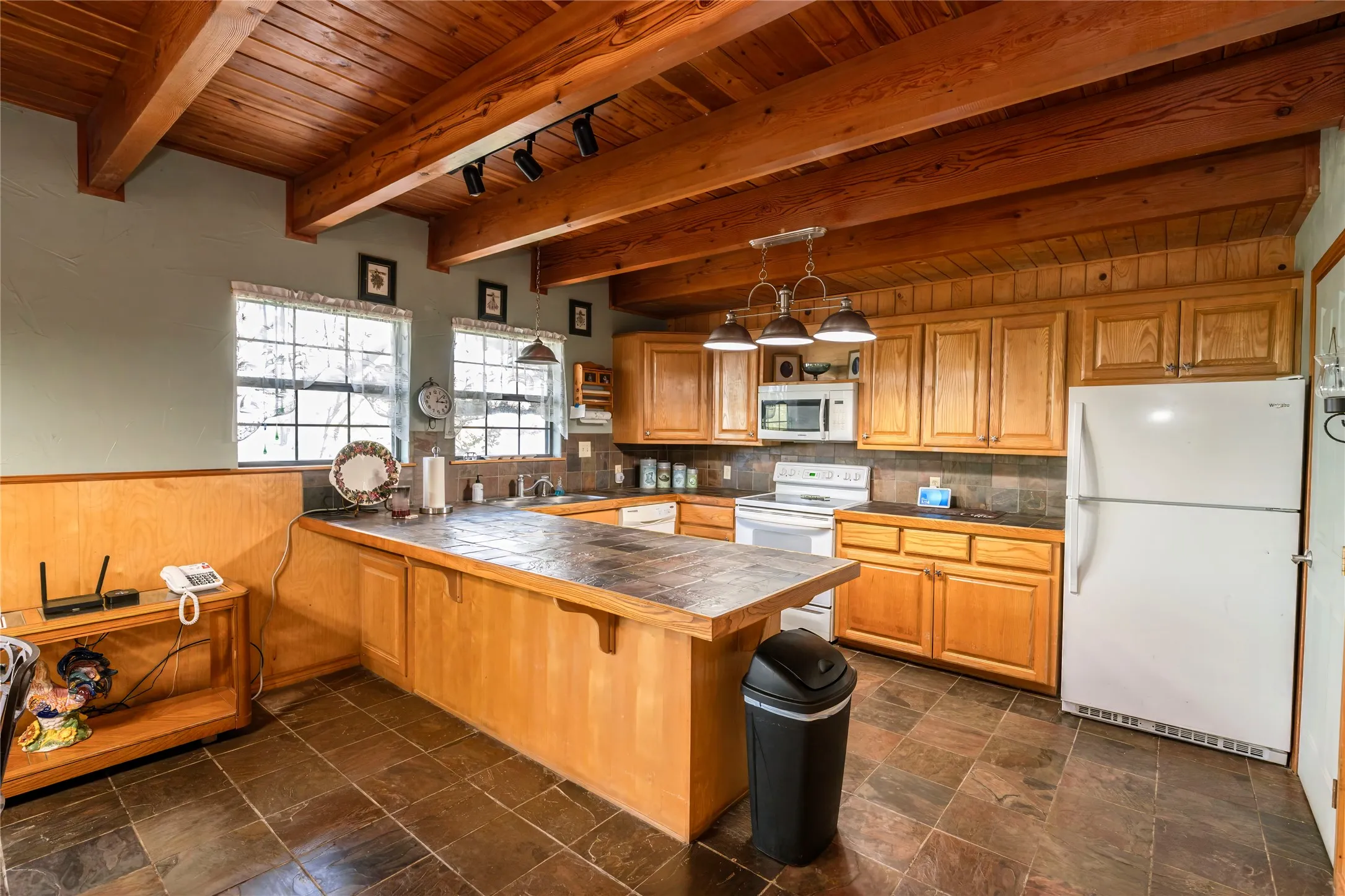 Kitchen with white appliances, pendant lighting, a wood ceiling with exposed beams, brown cabinetry, and a peninsula