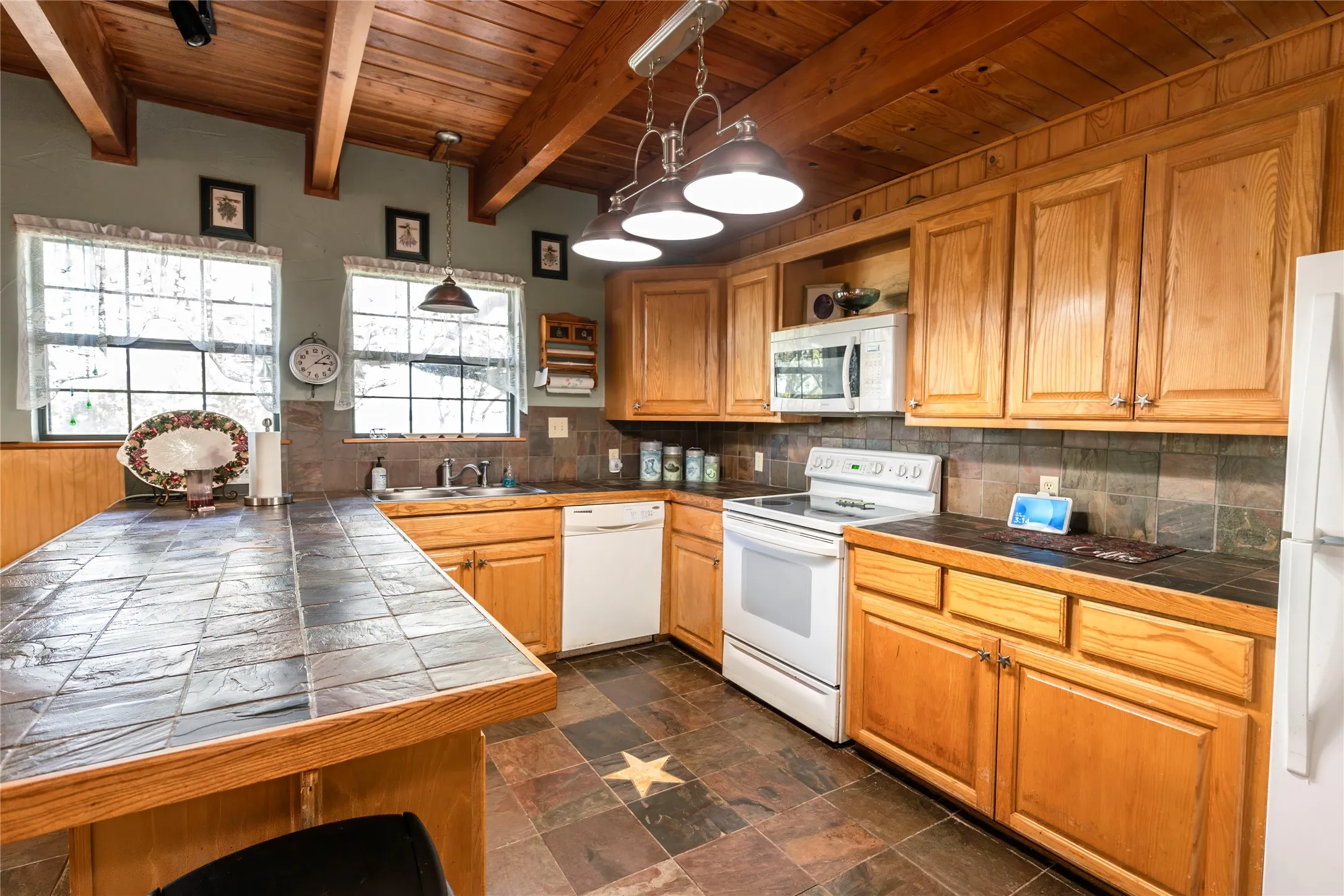 Kitchen featuring white appliances, a wood ceiling with exposed beams, pendant lighting, brown cabinets, and tasteful backsplash