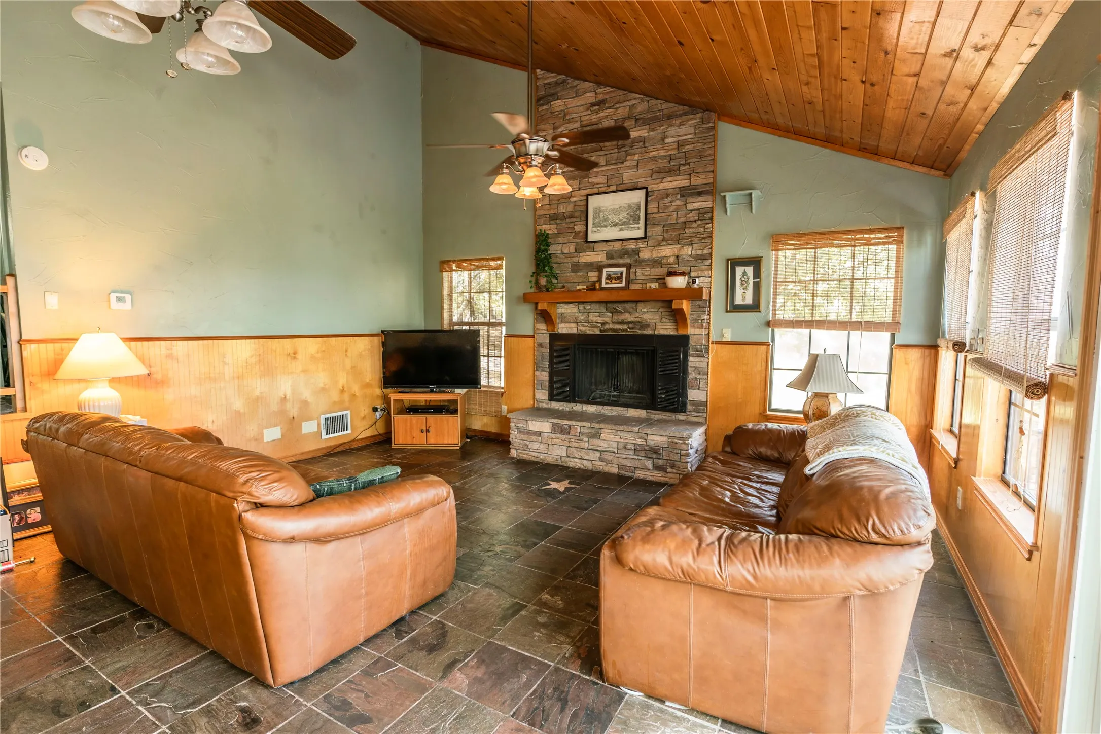 Living room featuring a wainscoted wall, wood walls, wood ceiling, a fireplace, and stone tile flooring
