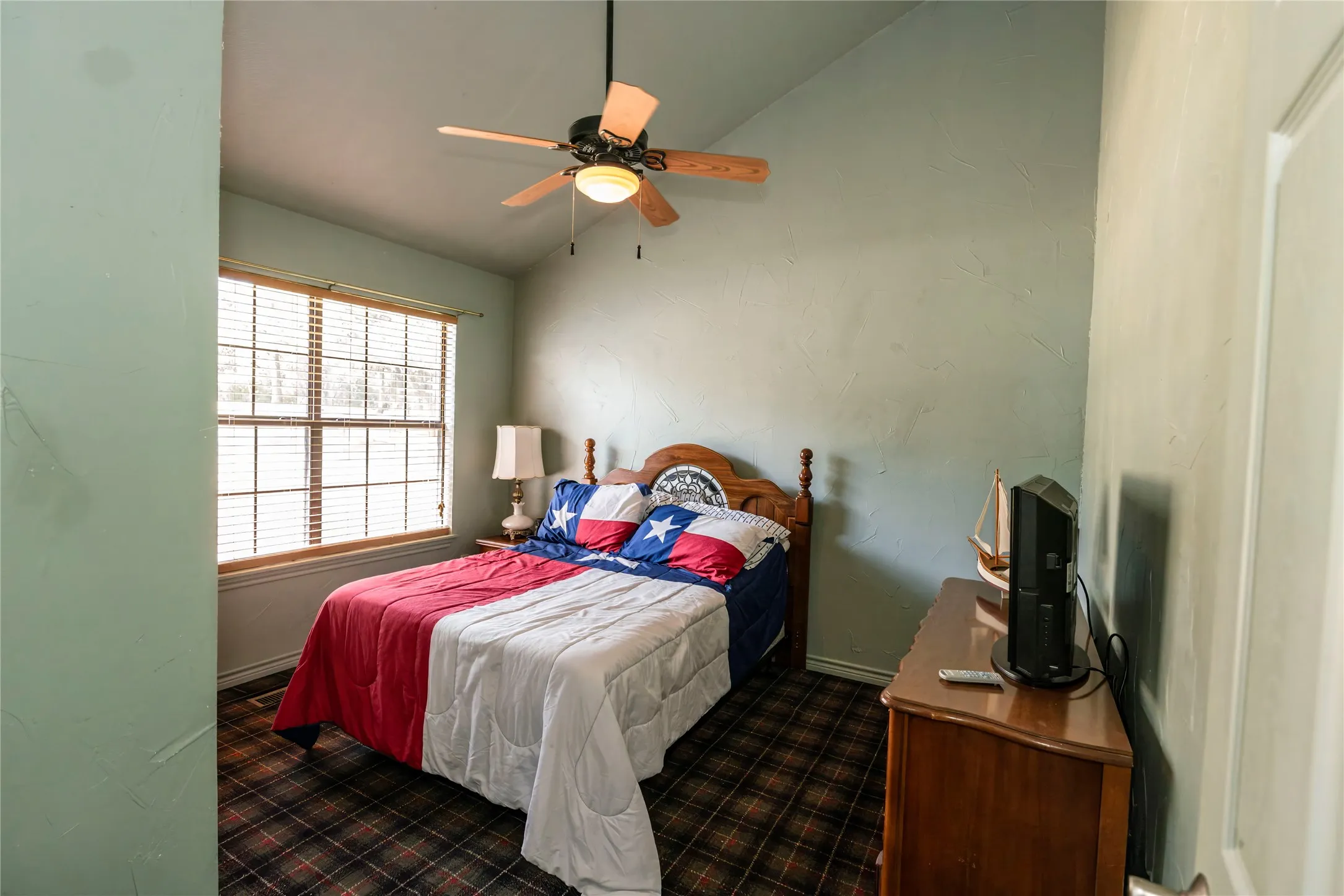 Bedroom with dark carpet, vaulted ceiling, and ceiling fan