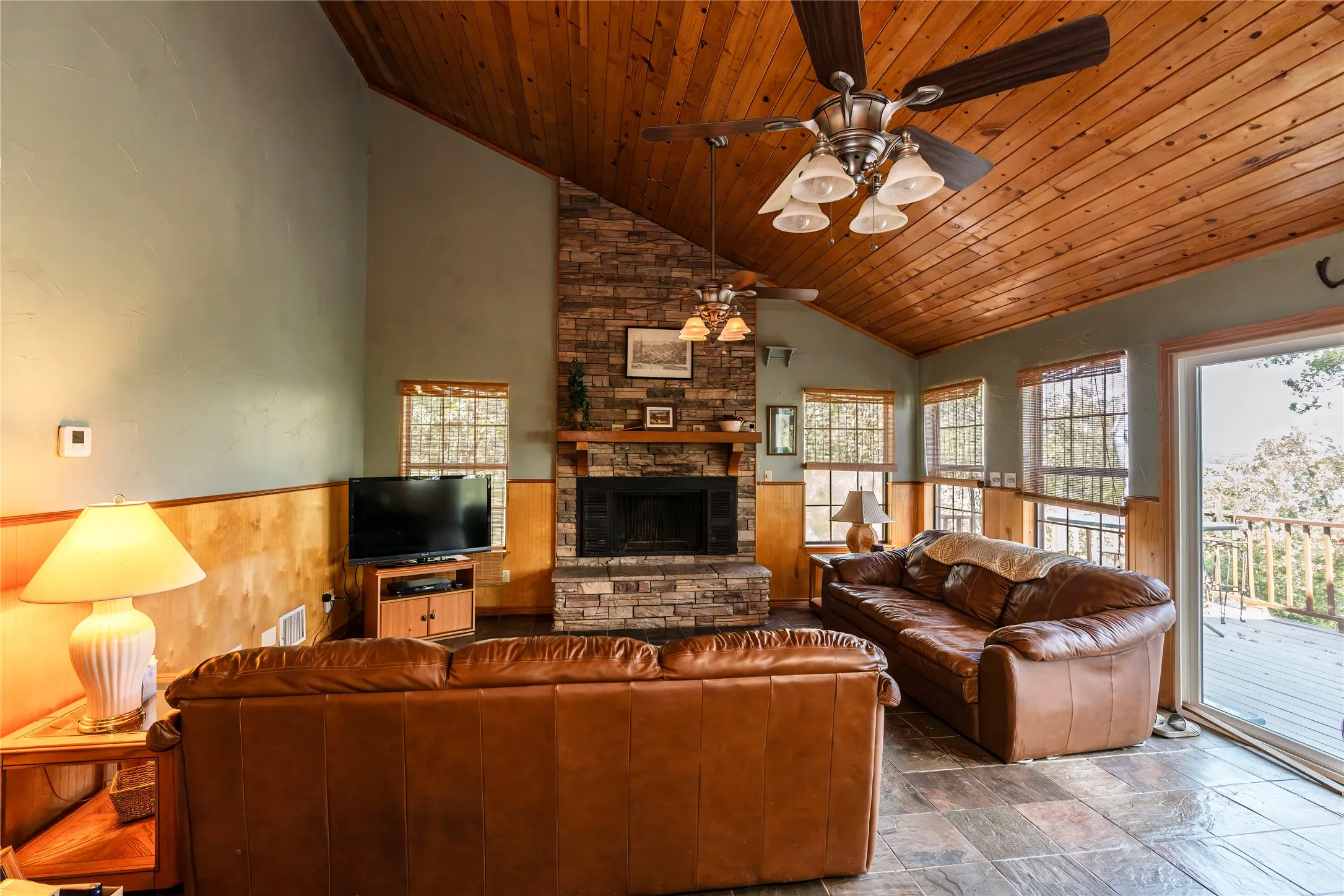 Living area featuring wainscoting, wooden ceiling, a stone fireplace, wood walls, and stone finish floors