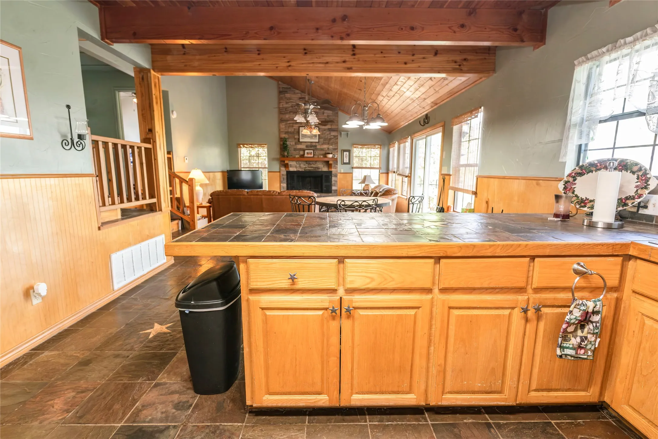 Kitchen with open floor plan, wainscoting, wooden walls, wooden ceiling, and a stone fireplace