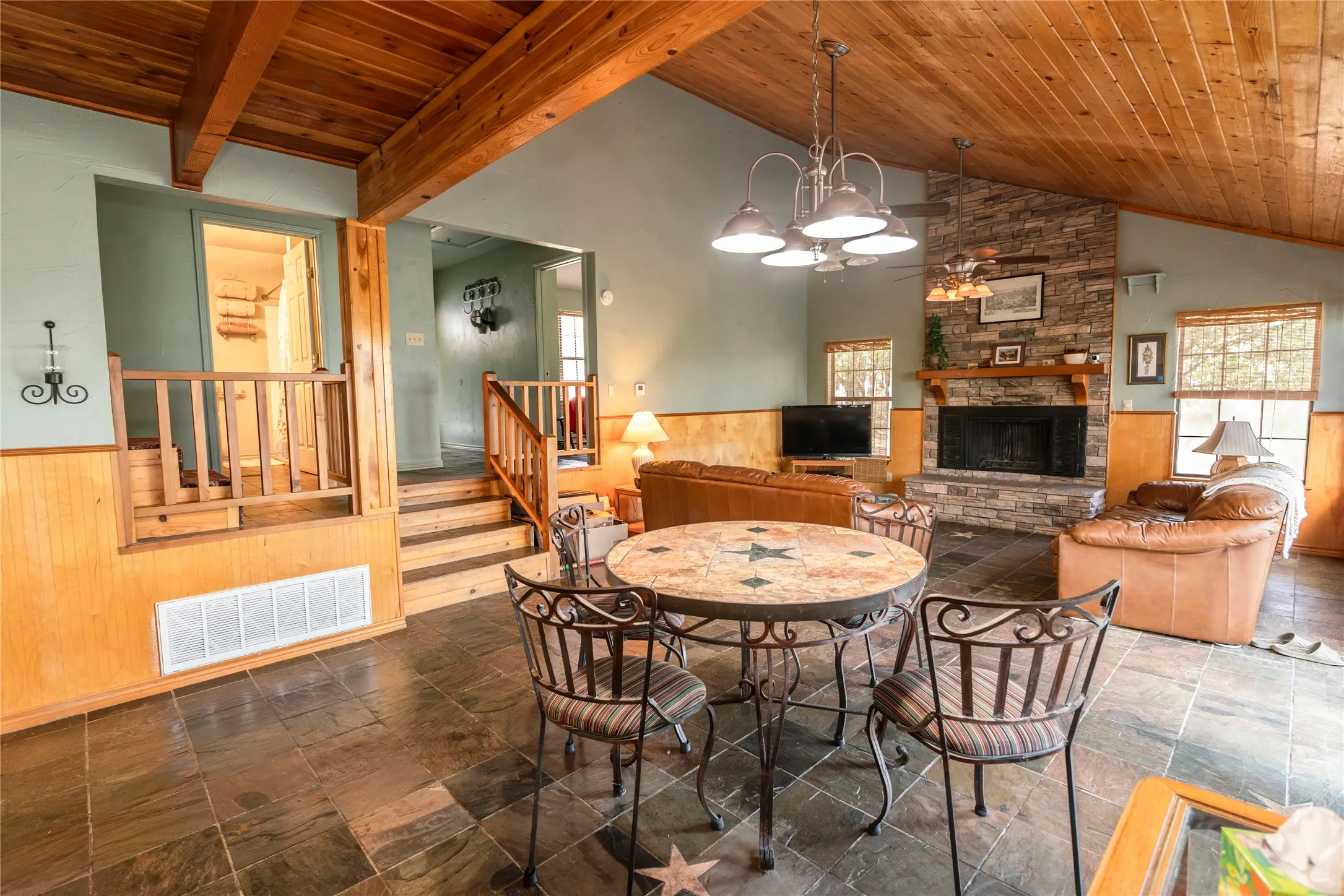 Dining space featuring wainscoting, wood walls, wooden ceiling, a fireplace, and a chandelier