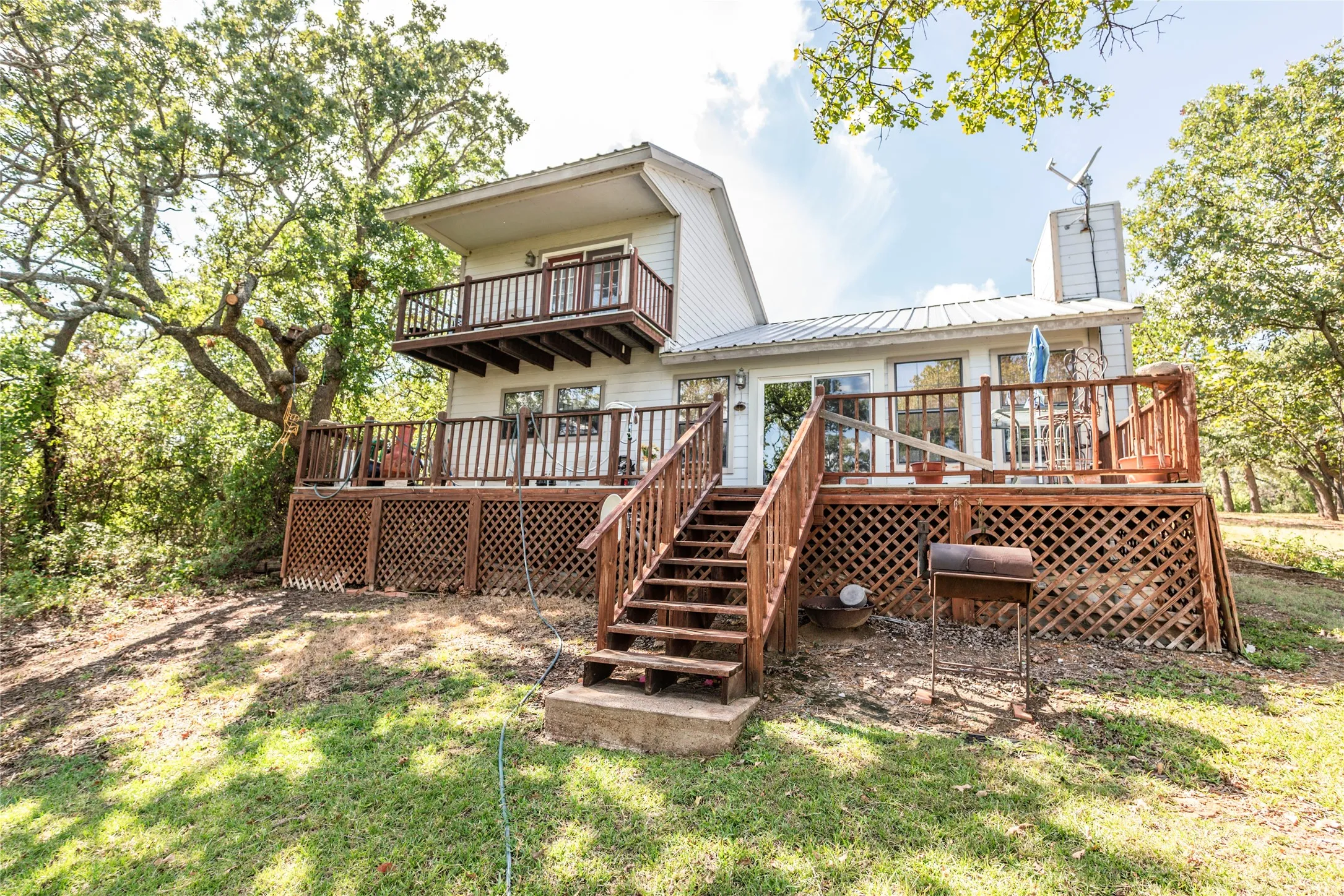Rear view of house featuring a deck, a chimney, a metal roof, stairway, and a balcony