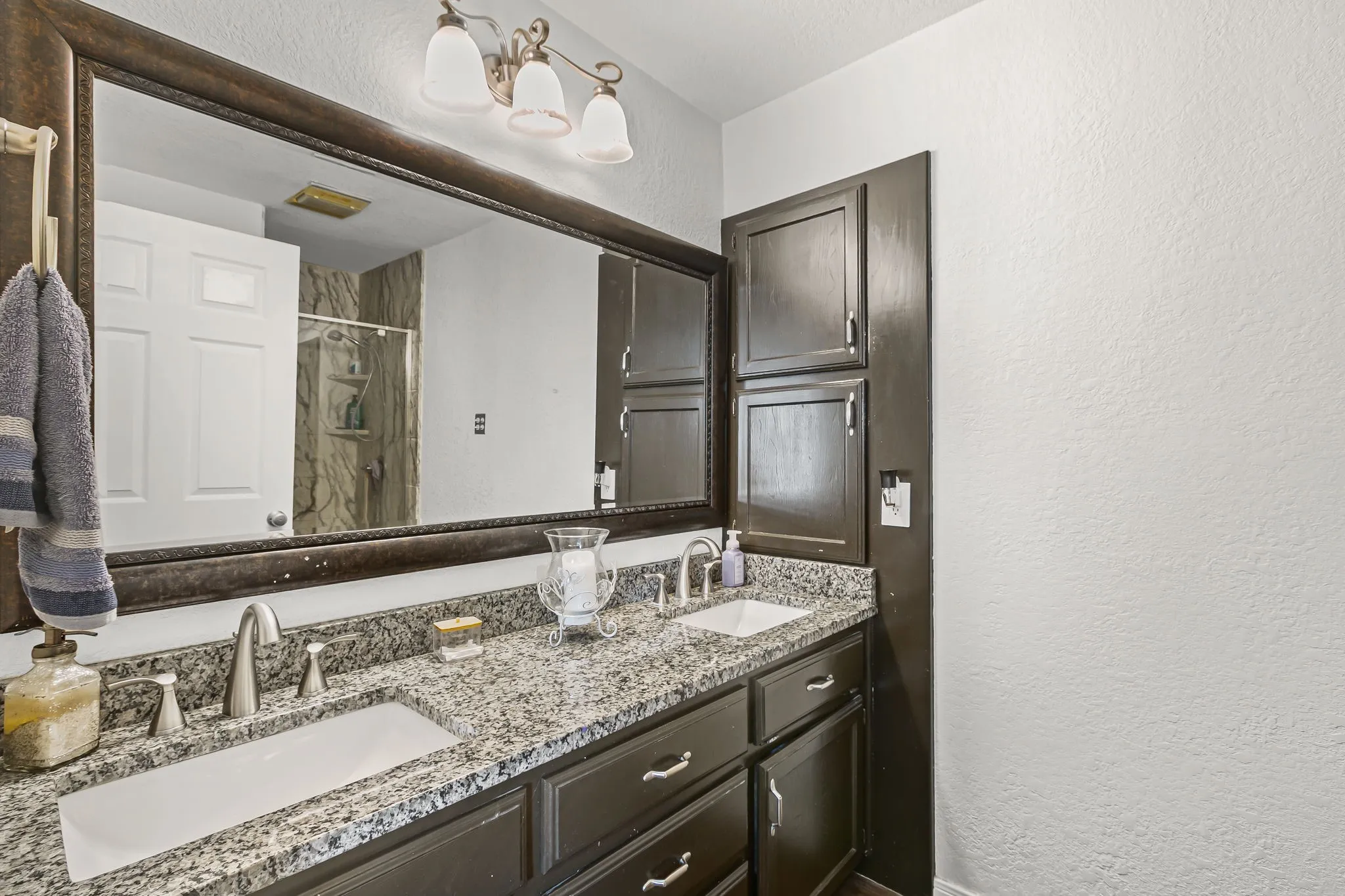 Bathroom with a textured wall, a shower stall, and double vanity
