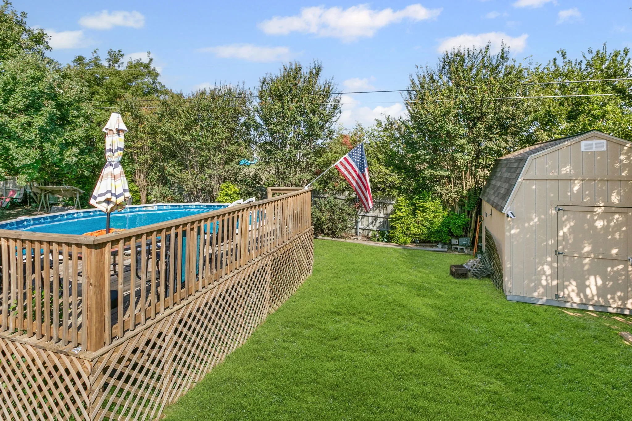 View of yard with a shed, a deck, an outdoor pool, and view of scattered trees