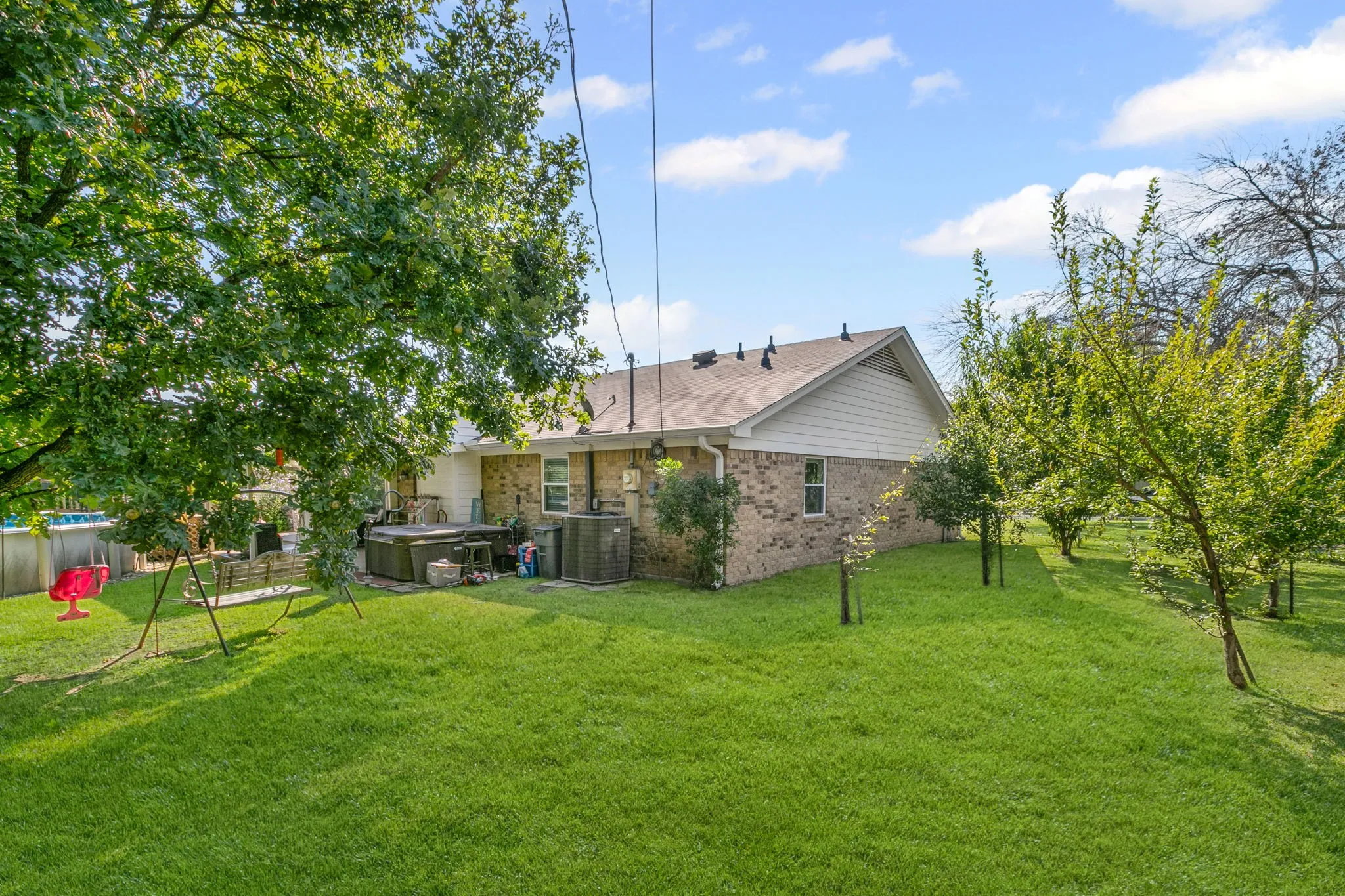 Back of property featuring brick siding, a hot tub, and roof with shingles