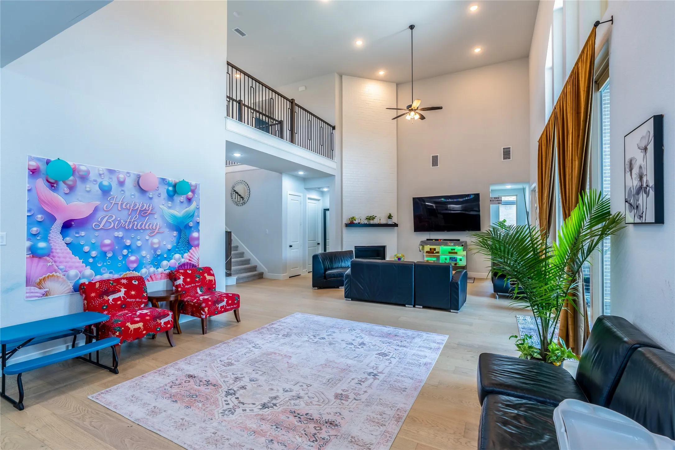 Living area featuring ceiling fan, a towering ceiling, stairs, light wood-style floors, and recessed lighting