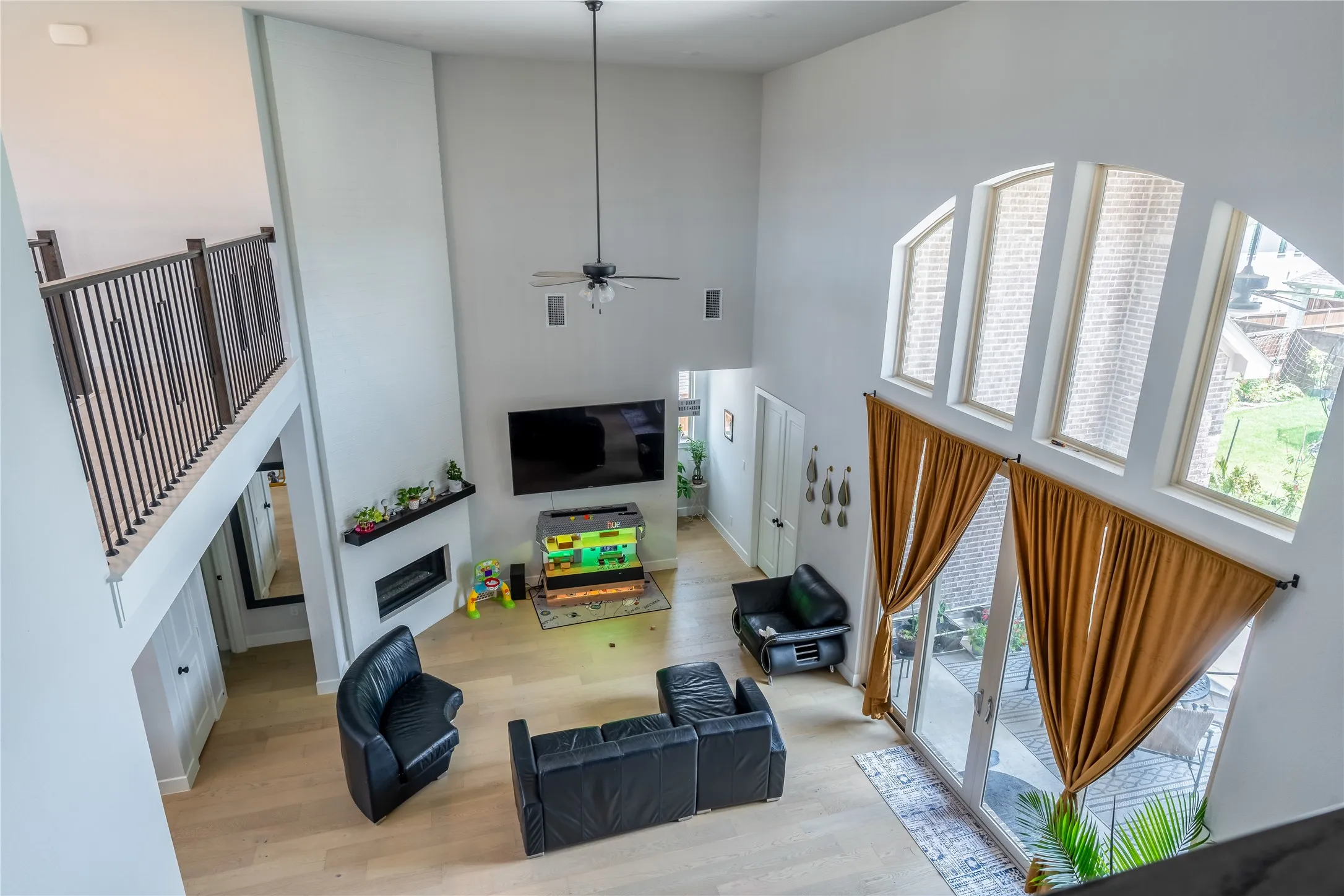 Living room featuring healthy amount of natural light, a towering ceiling, wood finished floors, ceiling fan, and a glass covered fireplace