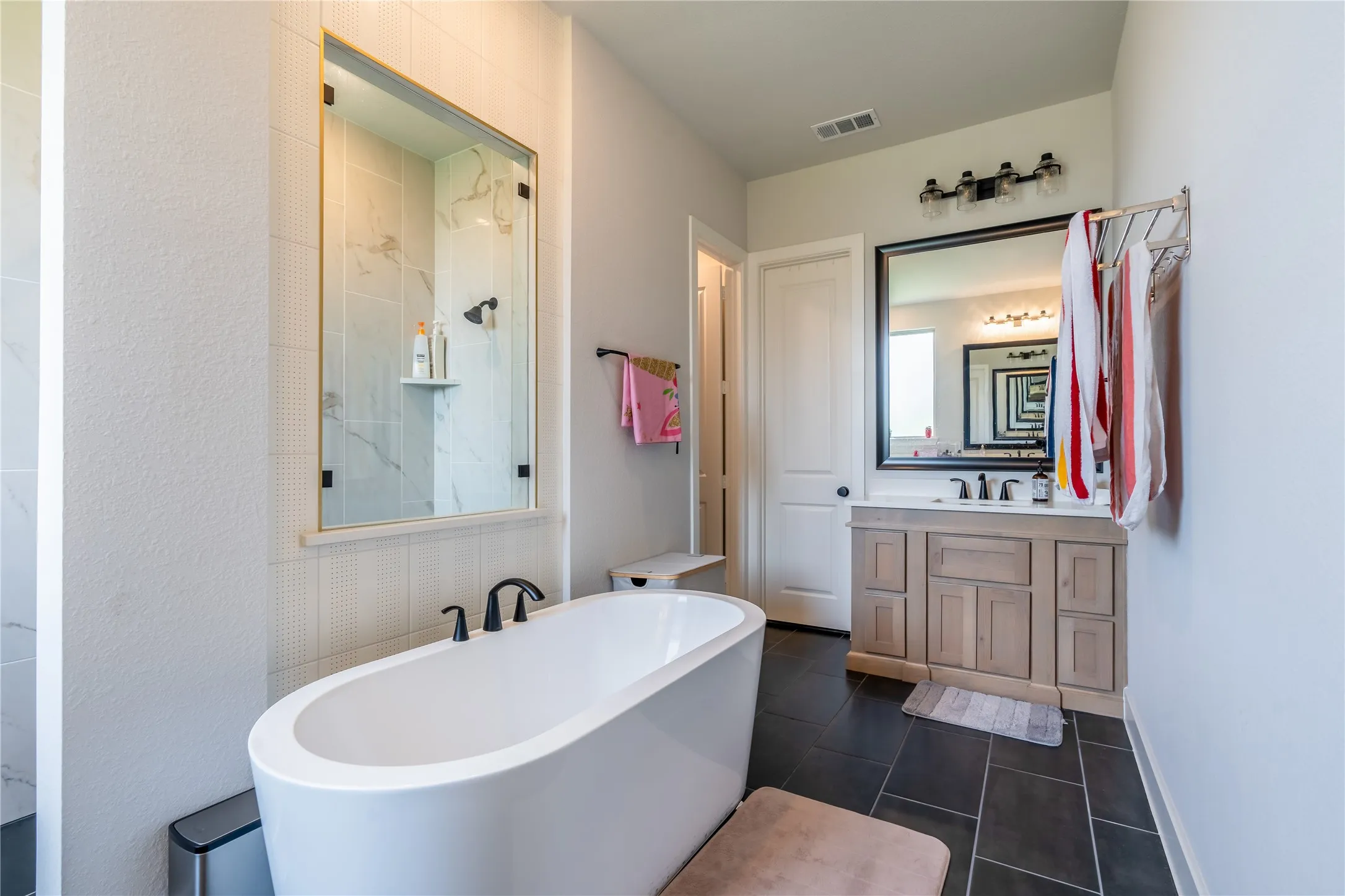 Bathroom with a freestanding bath, vanity, a marble finish shower, and dark tile patterned flooring