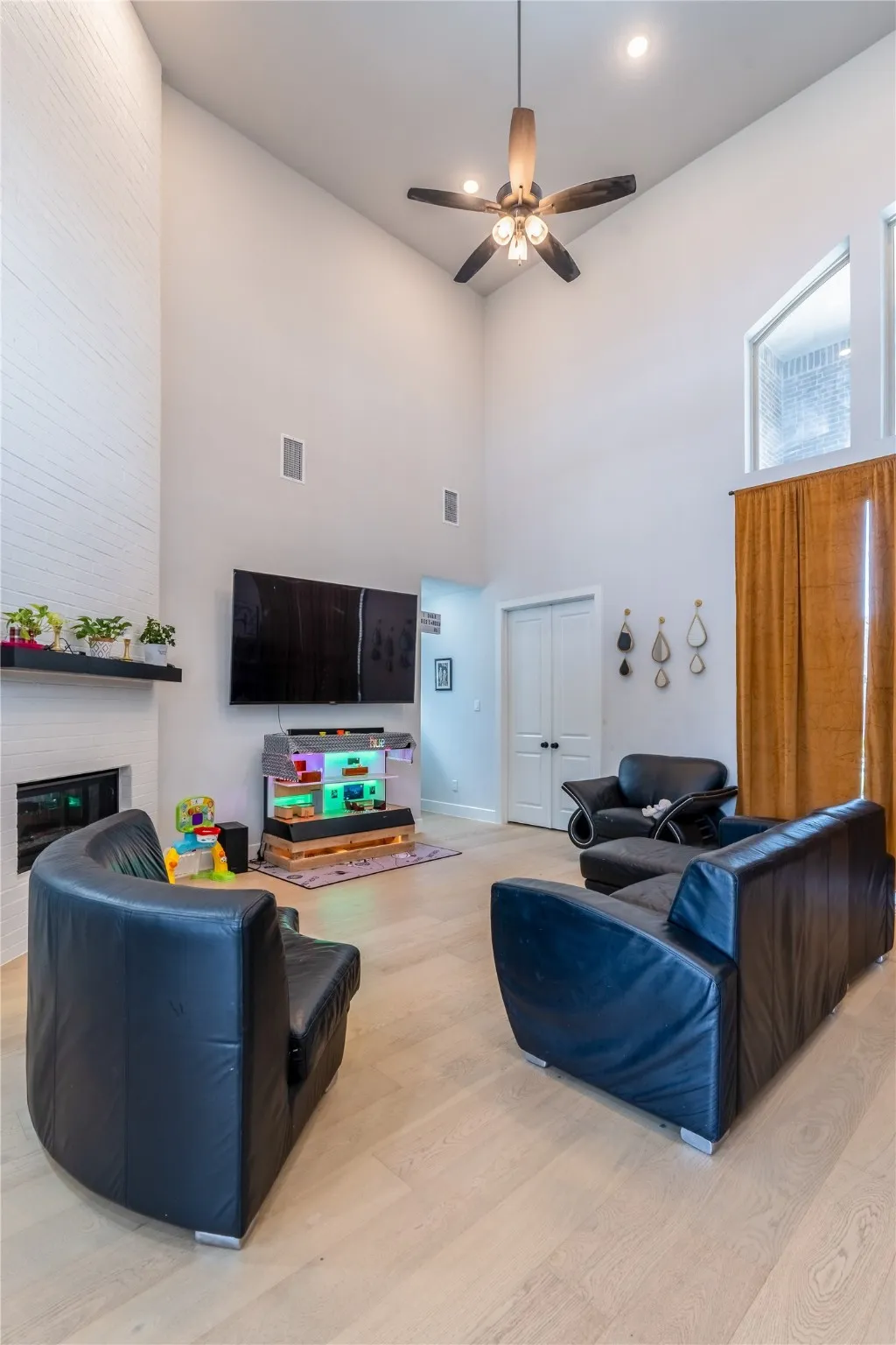 Living area featuring light wood-style floors, a towering ceiling, and ceiling fan