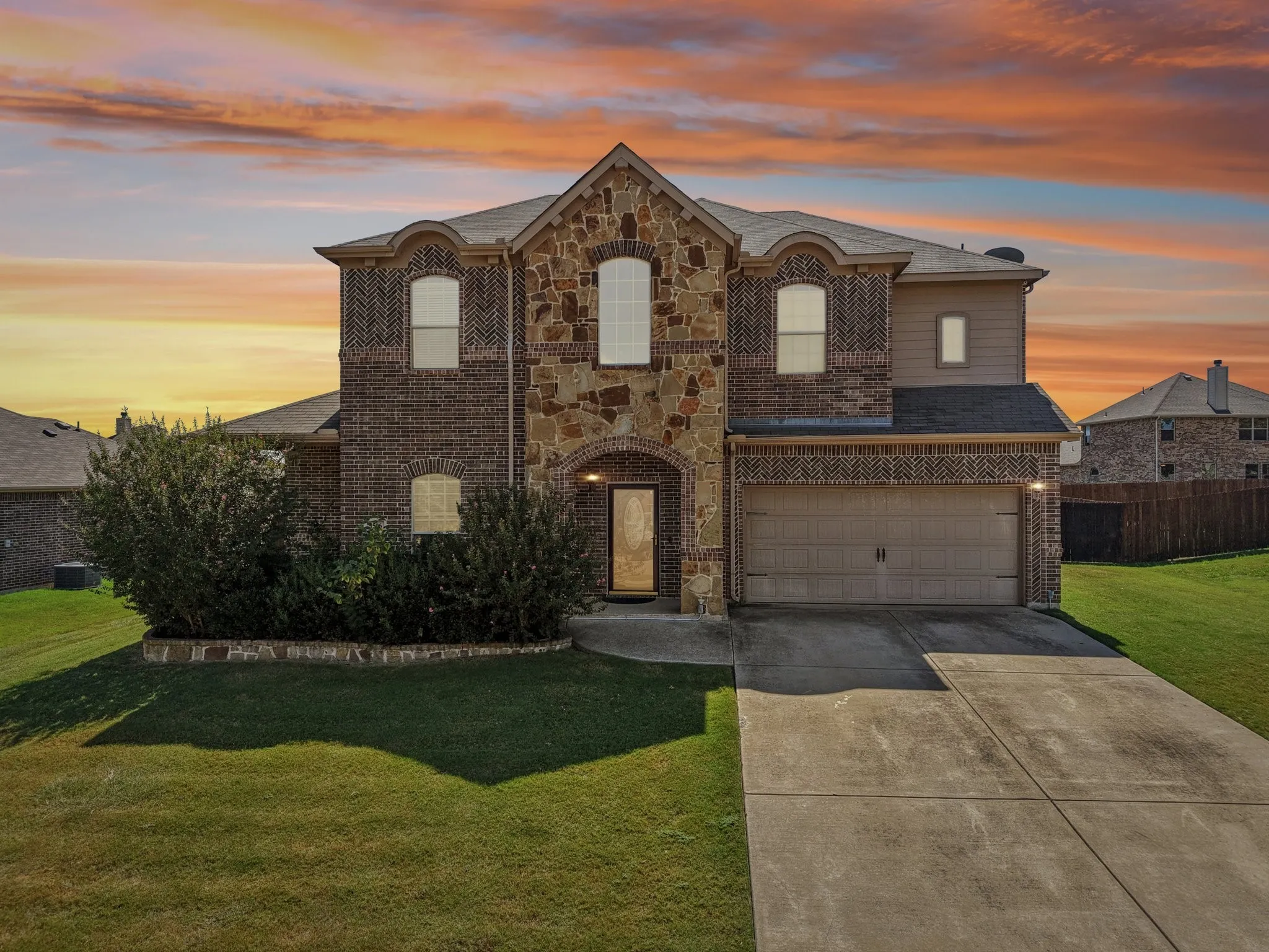 French country inspired facade with stone siding, brick siding, a yard, driveway, and an attached garage