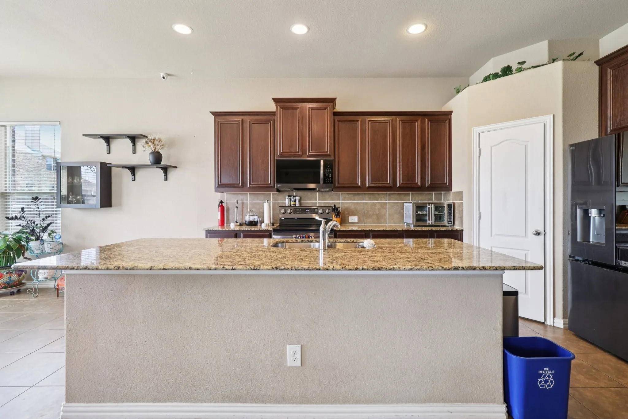 Kitchen featuring light tile patterned floors, backsplash, stainless steel appliances, light stone countertops, and open shelves