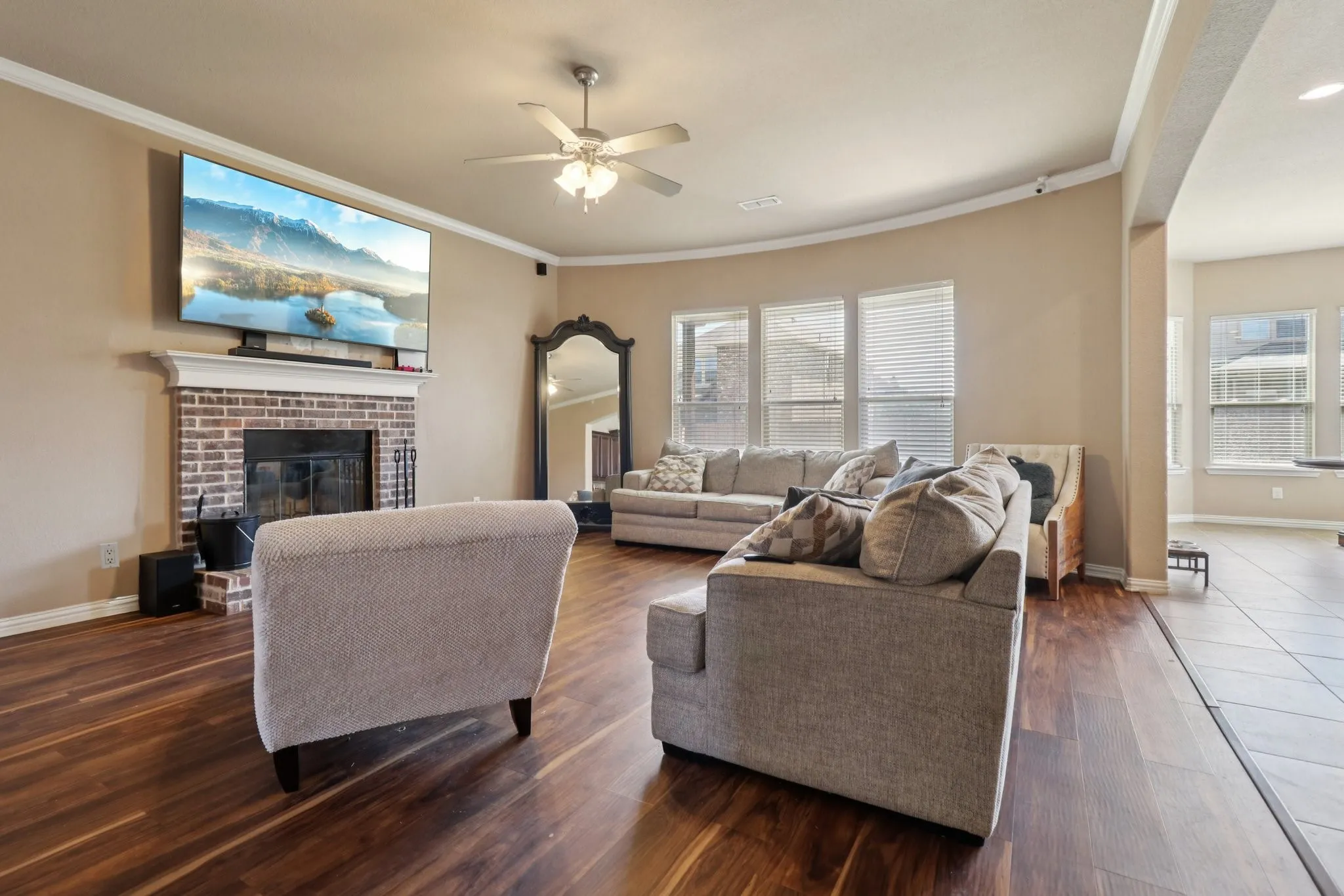 Living area with ornamental molding, a brick fireplace, dark wood-type flooring, and ceiling fan