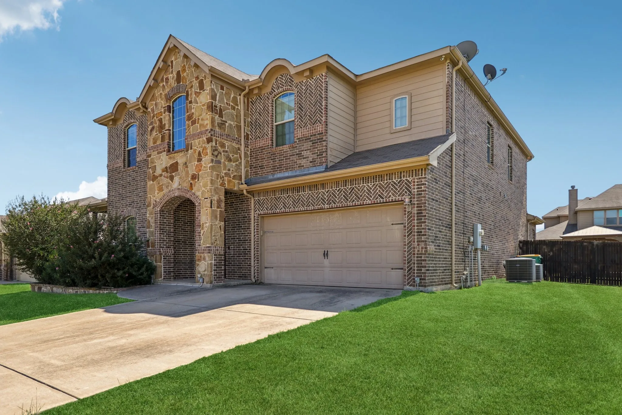 View of front facade with stone siding, concrete driveway, a front yard, an attached garage, and brick siding