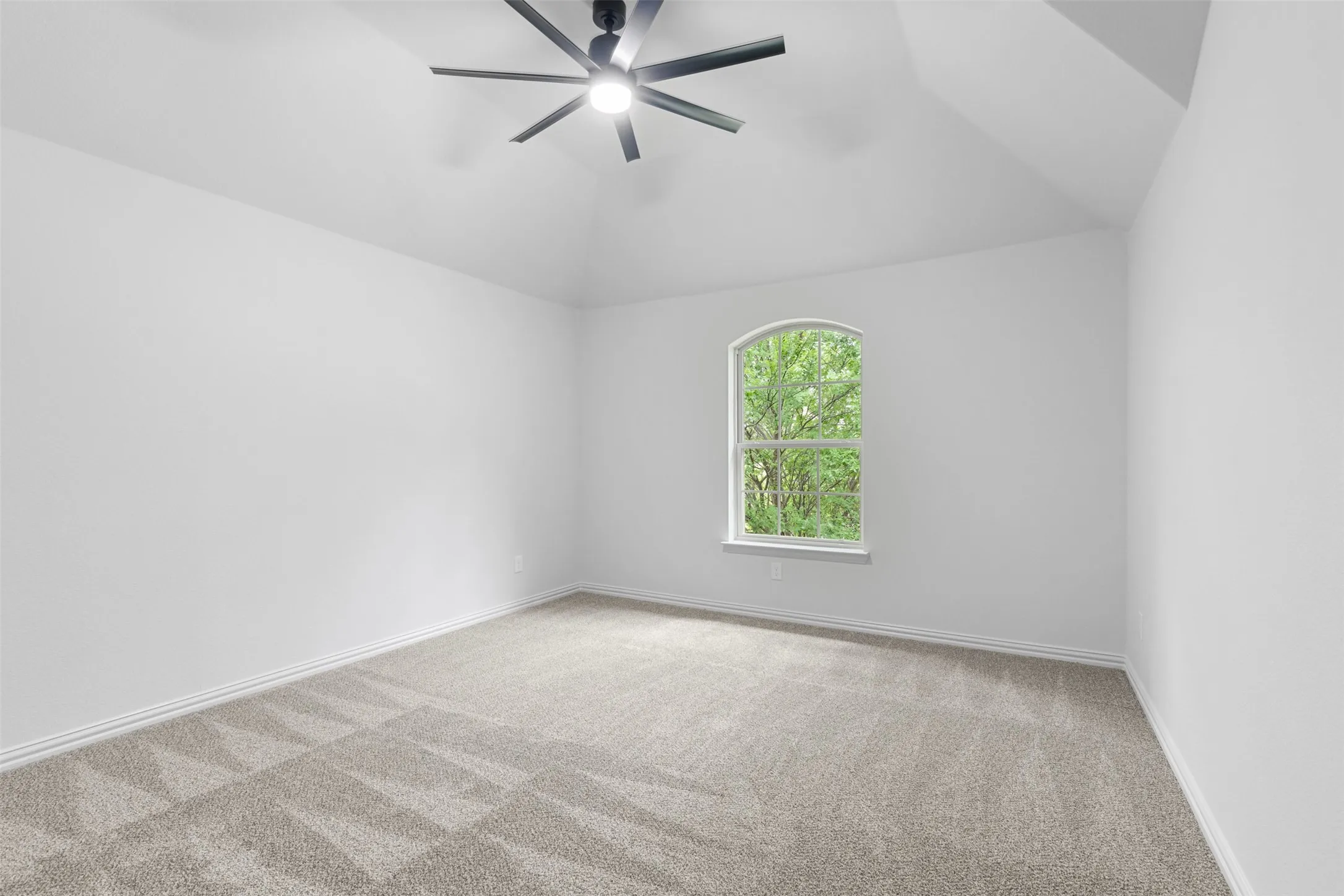 Carpeted spare room featuring lofted ceiling, a ceiling fan, and baseboards