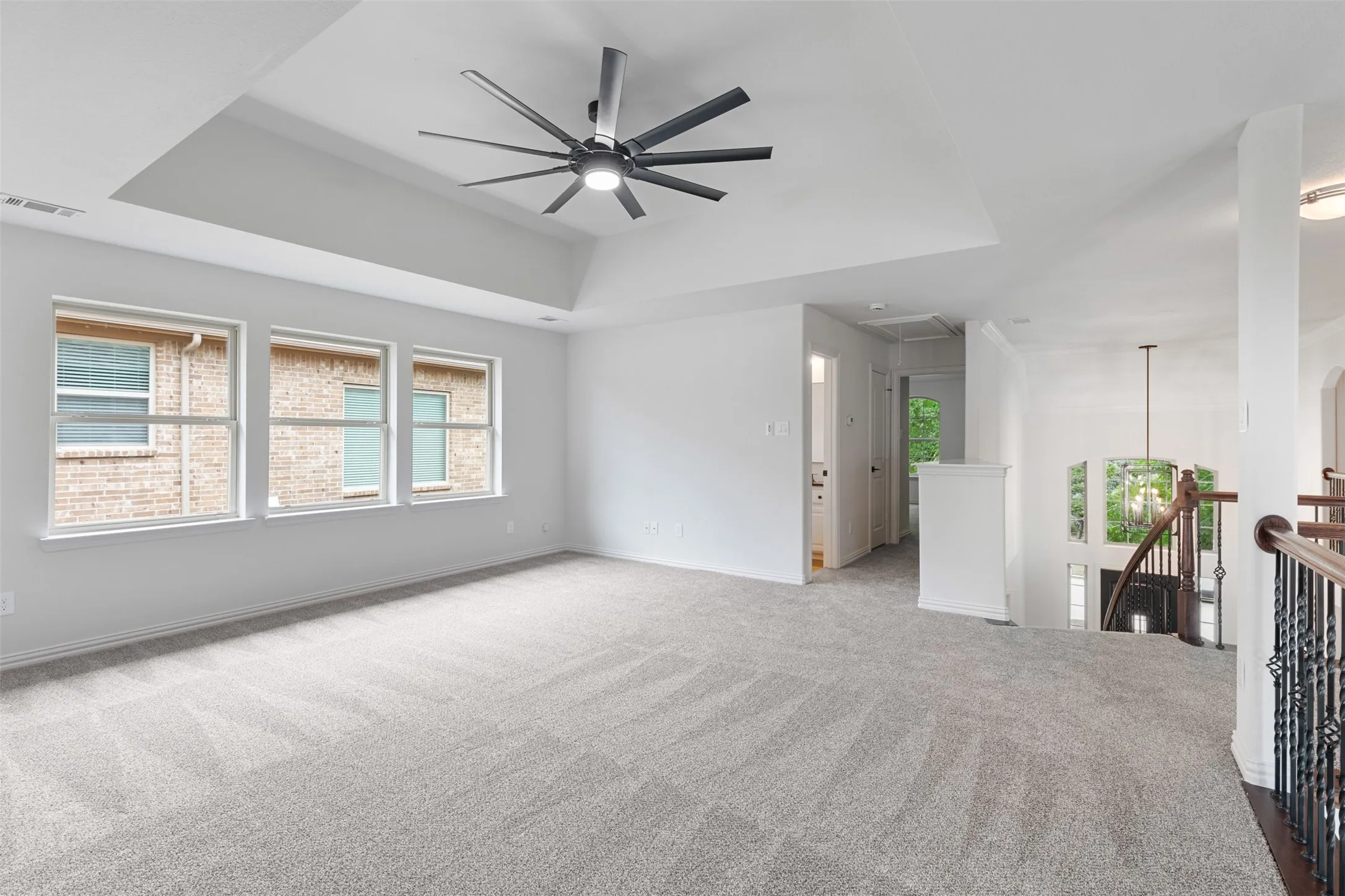 Unfurnished living room with attic access, a tray ceiling, a ceiling fan, visible vents, and carpet floors