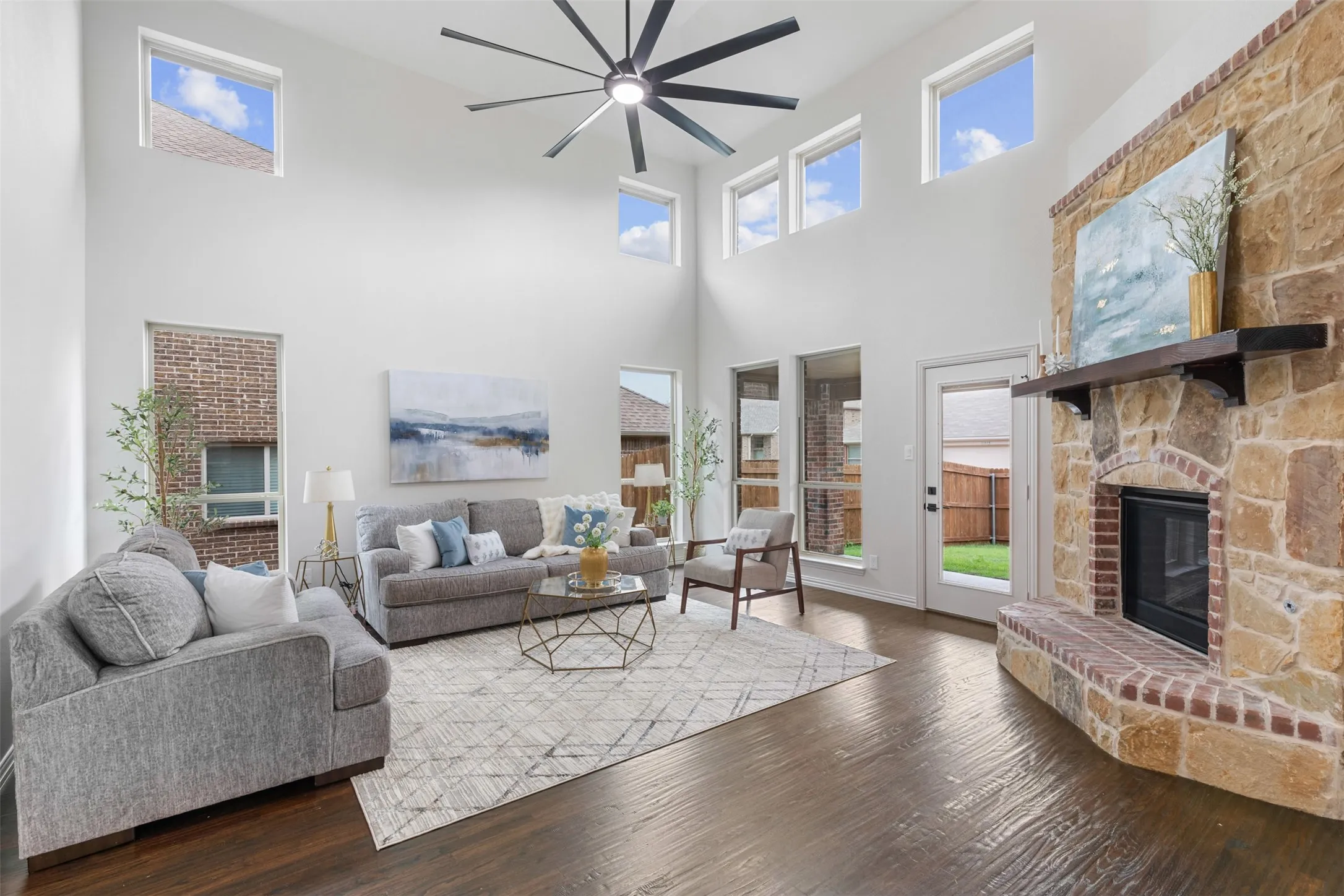 Living area with a high ceiling, a ceiling fan, wood finished floors, and a fireplace