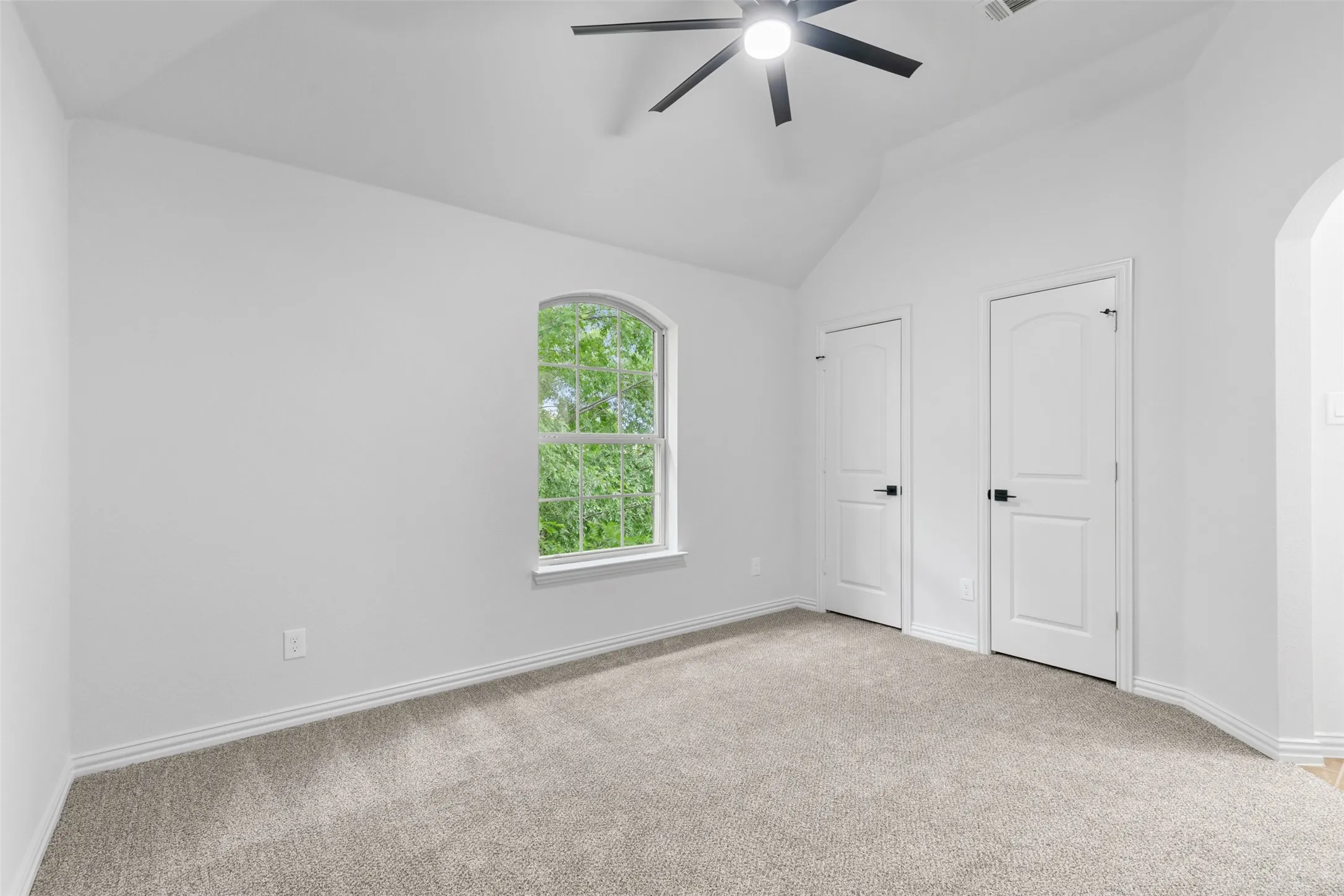 Unfurnished bedroom with arched walkways, vaulted ceiling, carpet, and baseboards