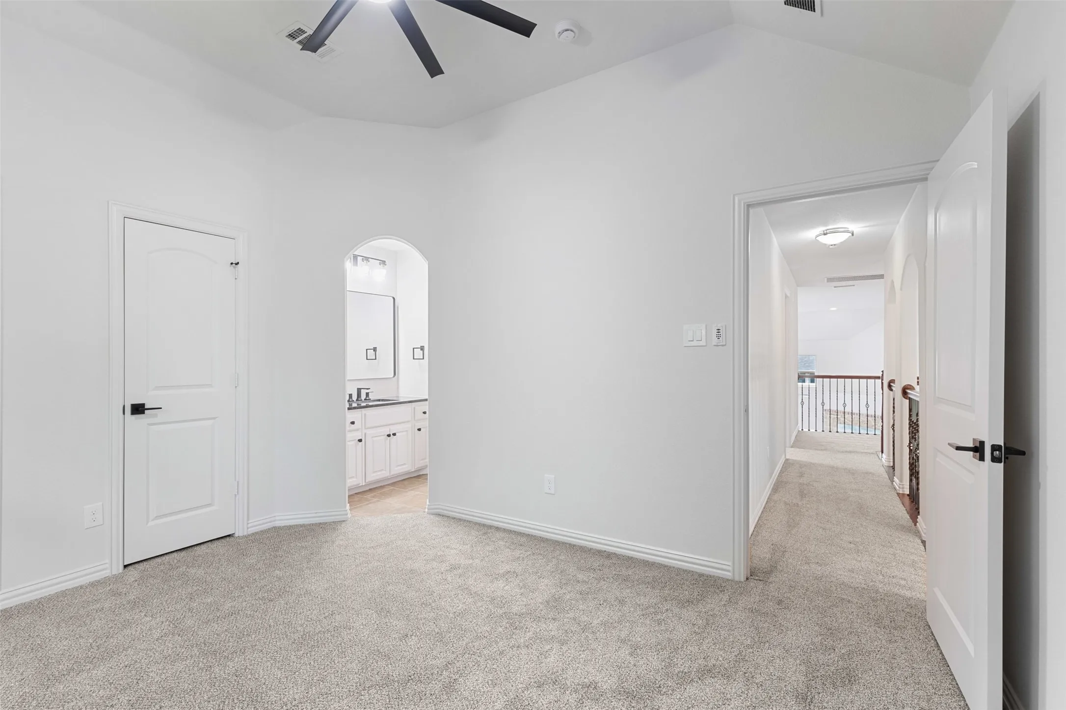 Unfurnished bedroom with arched walkways, ensuite bath, light colored carpet, visible vents, and lofted ceiling