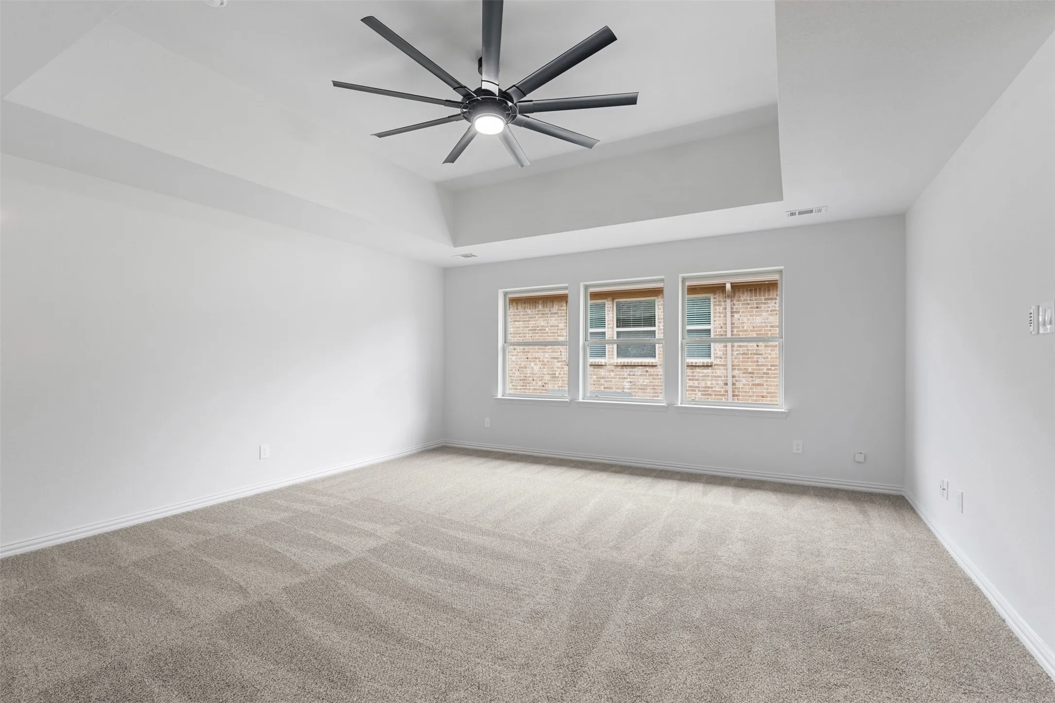 Carpeted spare room with baseboards, visible vents, a raised ceiling, and ceiling fan