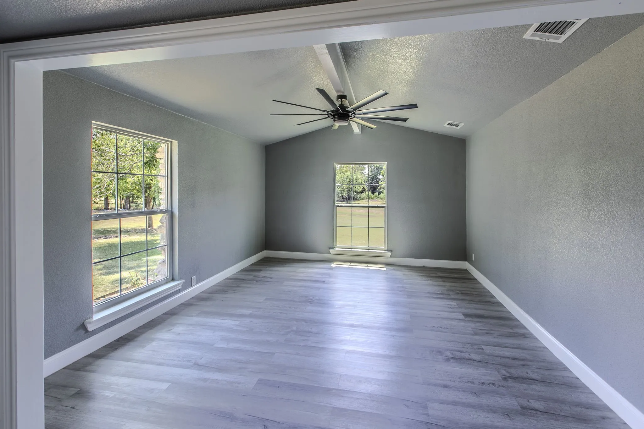 Empty room featuring a textured wall, wood finished floors, vaulted ceiling, a textured ceiling, and a ceiling fan