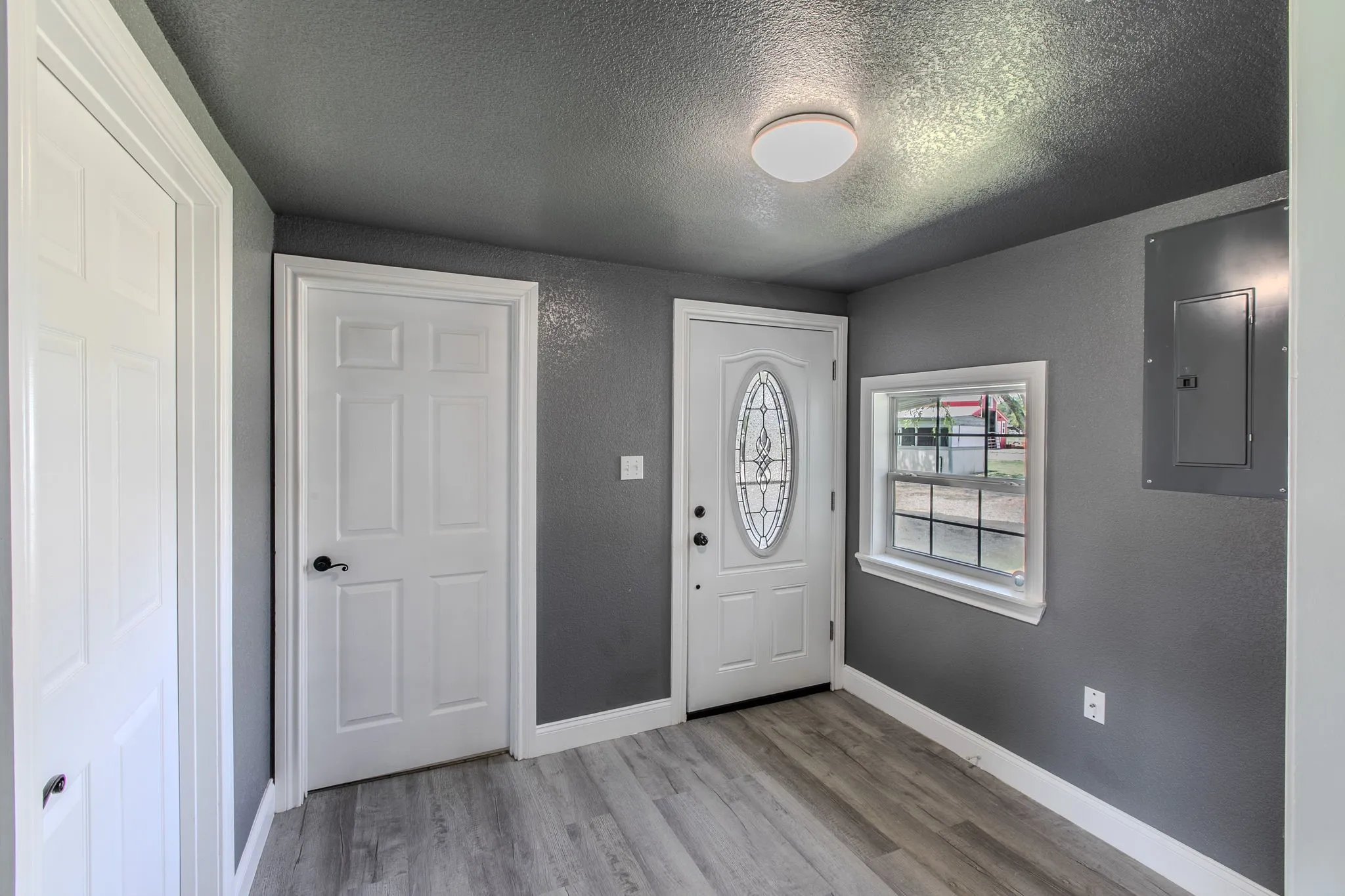 Foyer entrance featuring electric panel, light wood-type flooring, a textured ceiling, and a textured wall