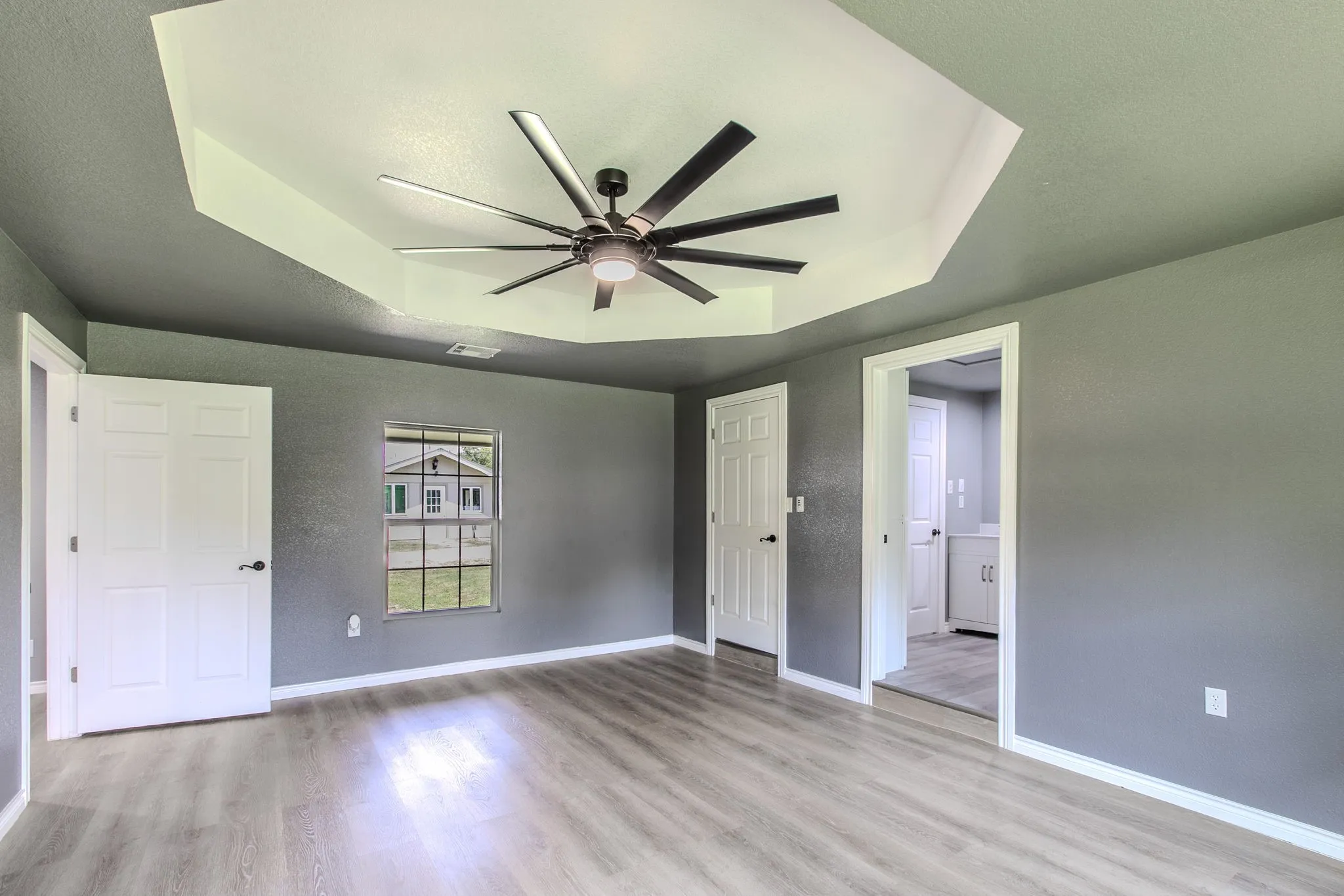 Unfurnished bedroom featuring a tray ceiling, light wood-style flooring, ceiling fan, and a textured ceiling