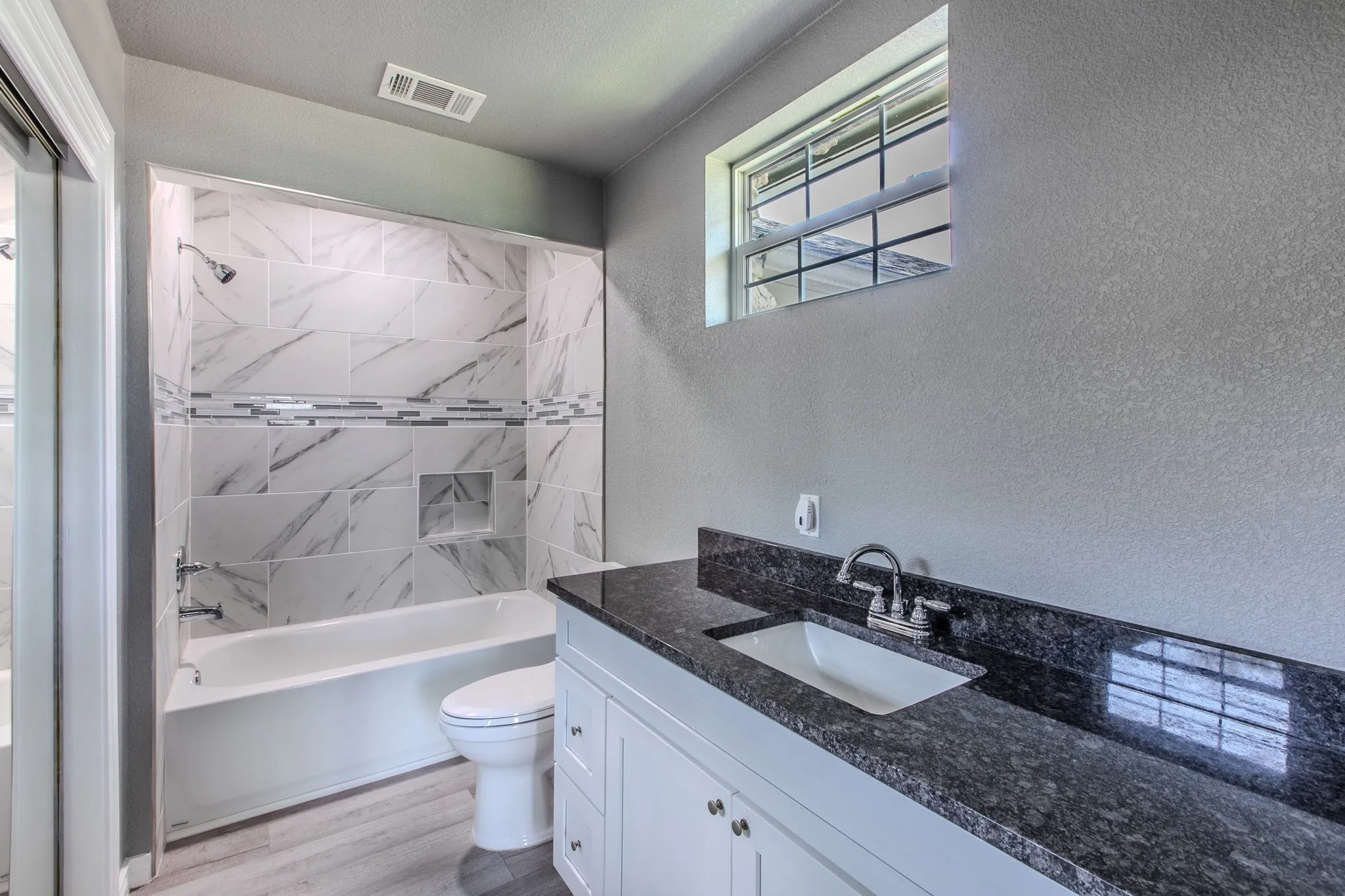 Bathroom with a textured wall, shower / bathtub combination, vanity, and light wood-style flooring
