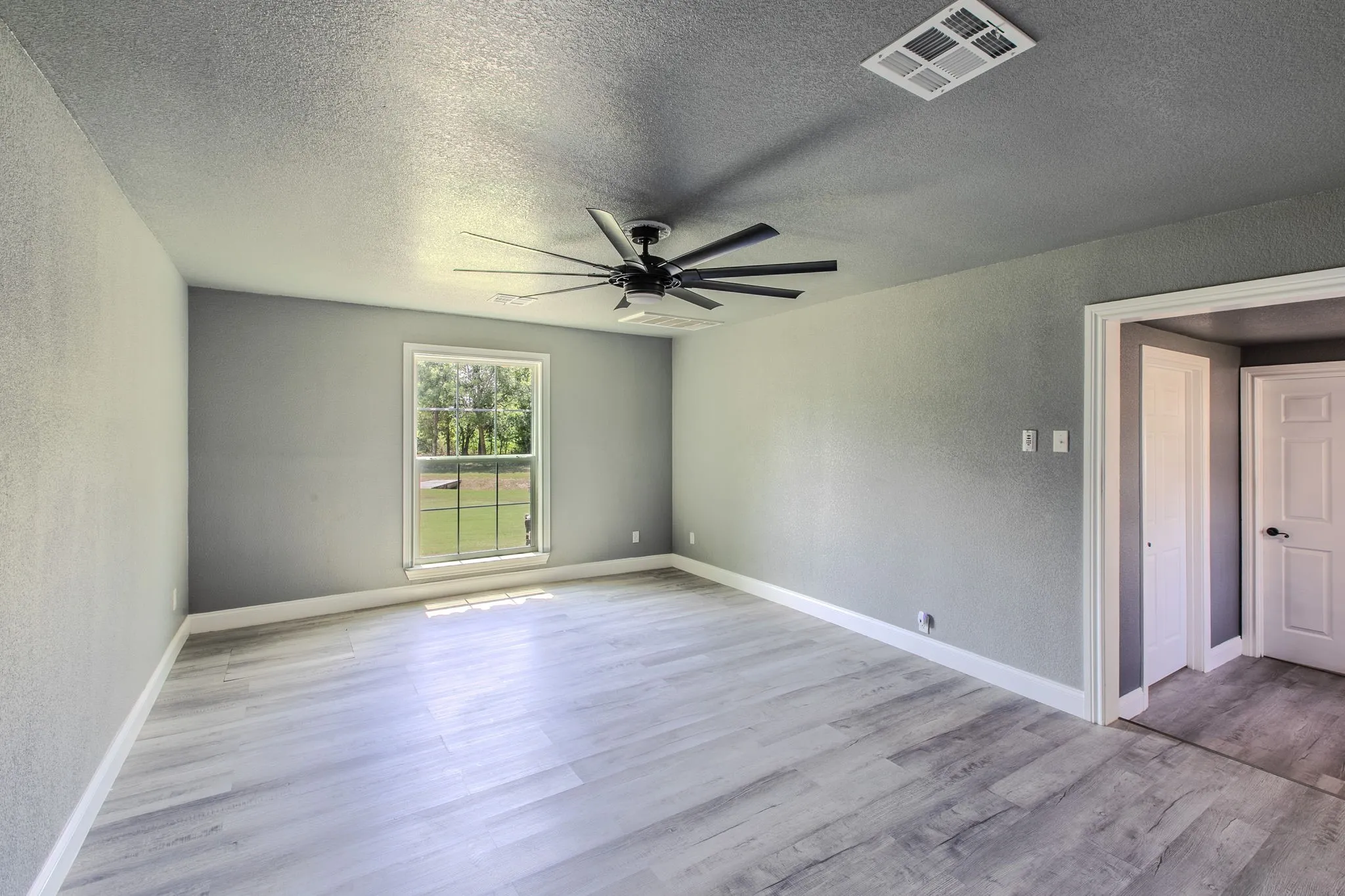 Empty room with a textured wall, a textured ceiling, light wood-style floors, and ceiling fan