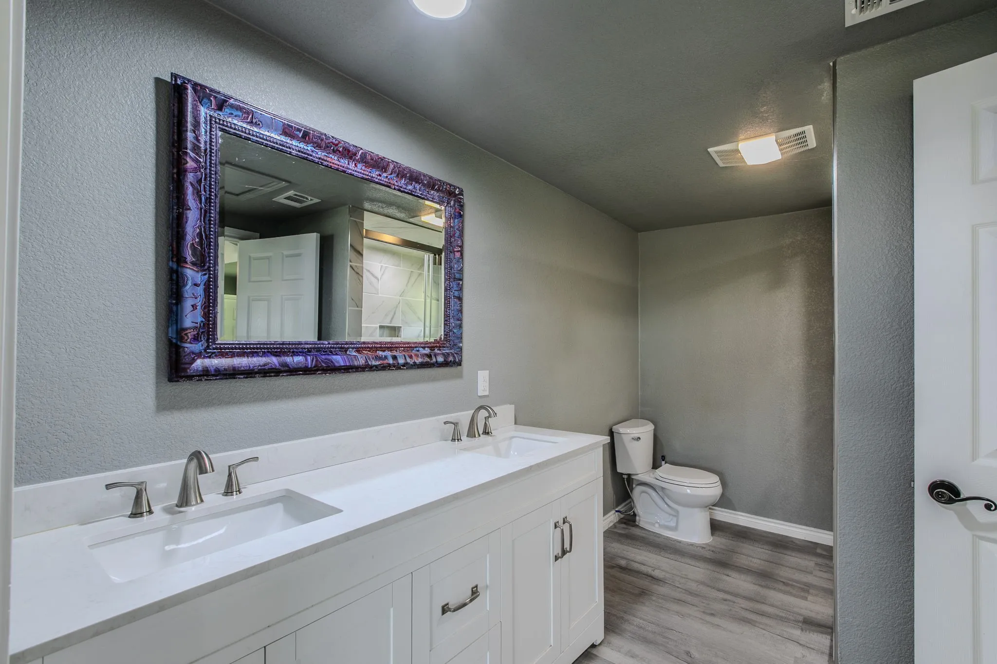 Bathroom featuring a textured wall, double vanity, and light wood-style floors