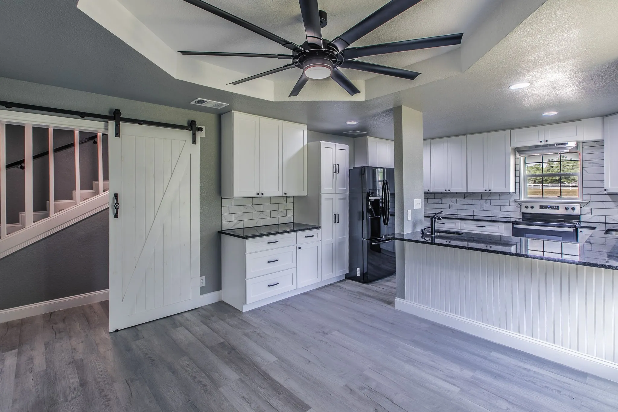 Kitchen featuring white cabinetry, black fridge with ice dispenser, stainless steel electric stove, a ceiling fan, and light wood finished floors
