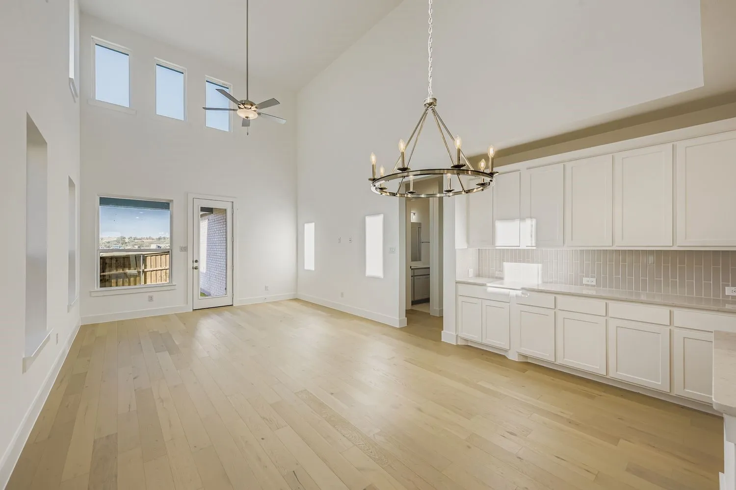 Unfurnished dining area with light wood finished floors, a towering ceiling, ceiling fan, a chandelier, and plenty of natural light