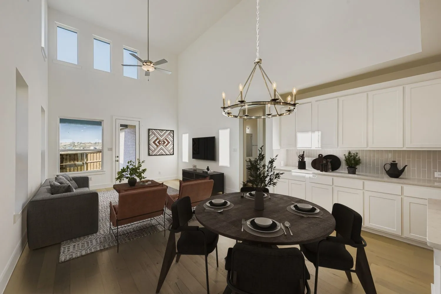 Virtually staged photo - Two-story vaulted ceilings, wood-finish flooring, white shaker cabinetry, tiled kitchen backsplash, and multiple windows
