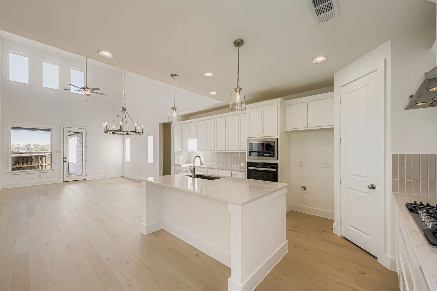 Kitchen featuring decorative backsplash, white cabinetry, pendant lighting, a center island with sink, and light wood-style flooring