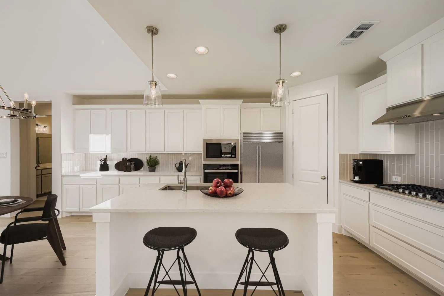 Virtually staged photo - Kitchen featuring white cabinetry, light-toned countertops, a full suite of stainless steel appliances, a center island with sink, and wood-finish flooring