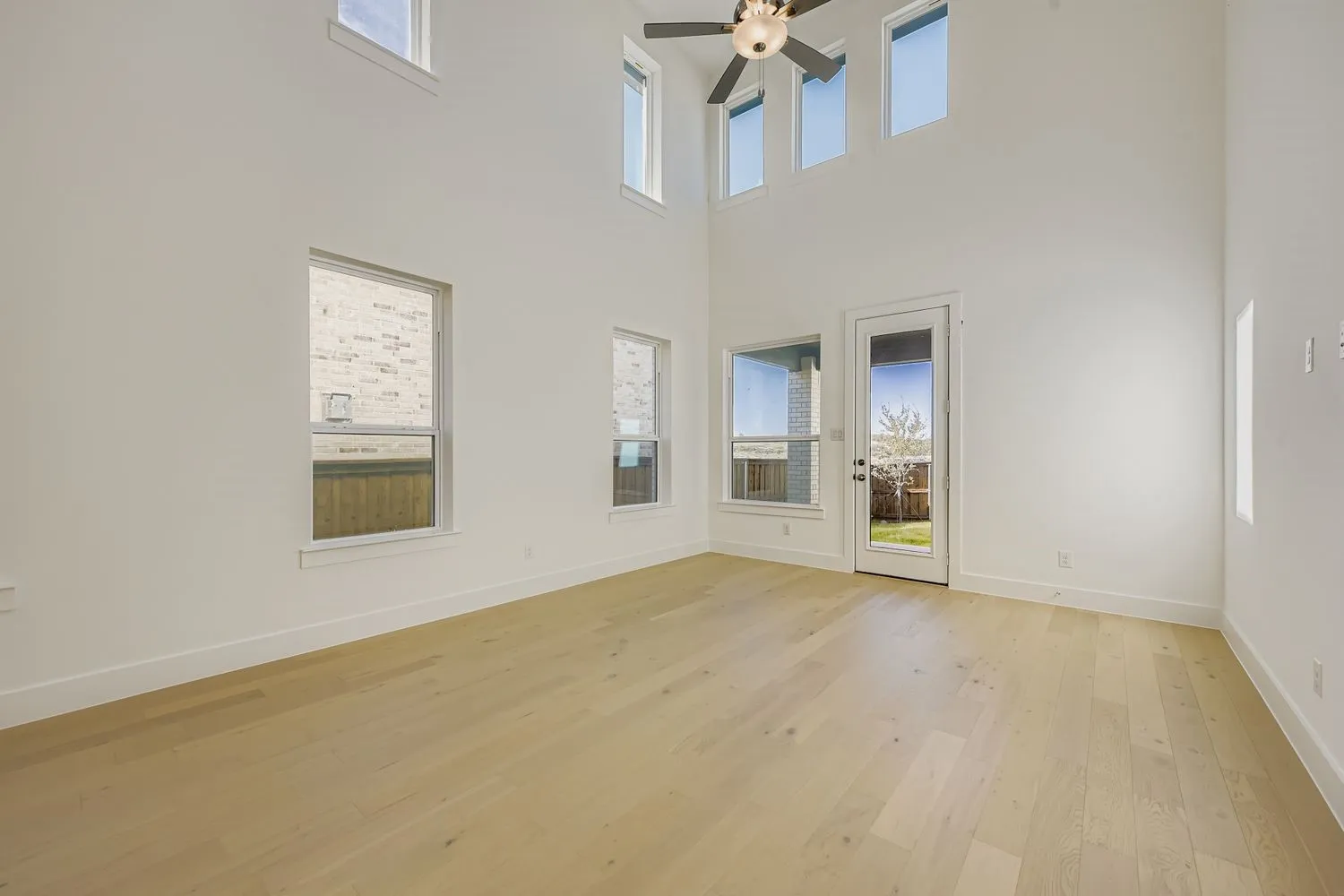 Spare room featuring light wood finished floors, a towering ceiling, and a ceiling fan