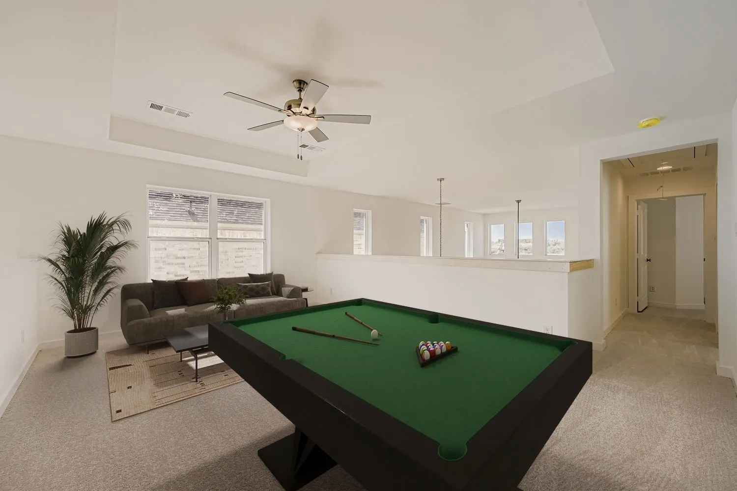 Virtually staged photo - Carpeted loft area featuring a ceiling fan, tray ceiling, multiple windows, and a knee wall with a wood-finish cap