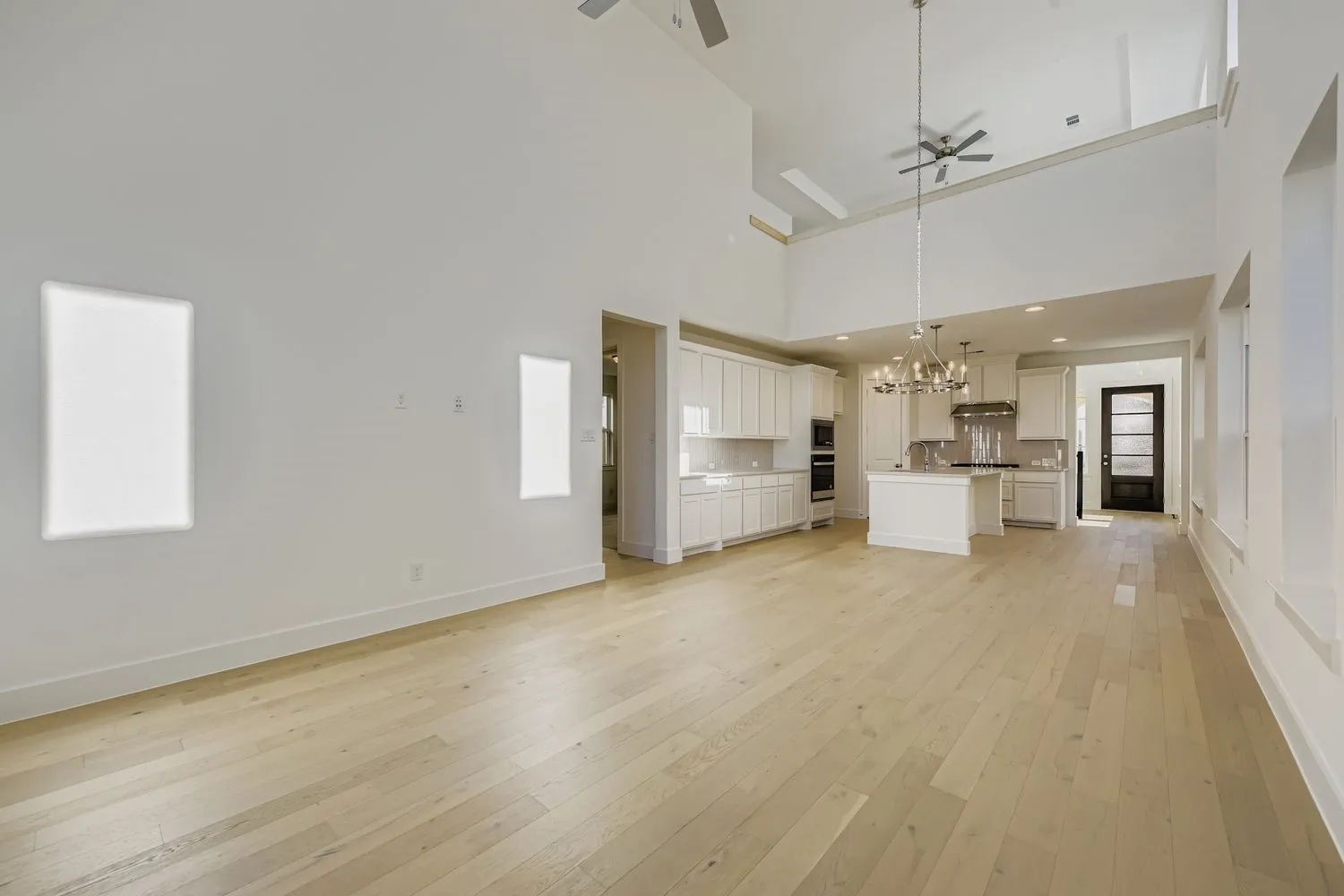 Unfurnished living room featuring light wood-style flooring, a chandelier, a ceiling fan, and a towering ceiling