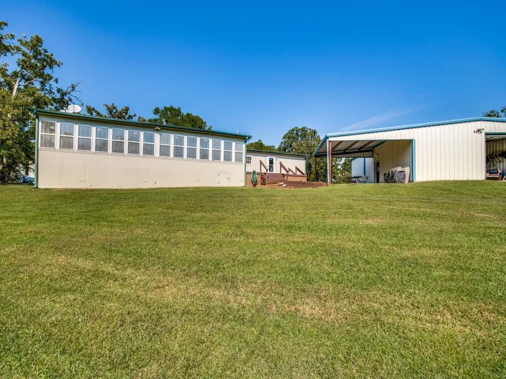 View of grassy yard featuring a pole building, an outbuilding, and a sunroom