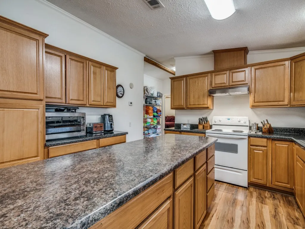 Kitchen featuring electric range, light wood-style floors, ornamental molding, a textured ceiling, and brown cabinetry
