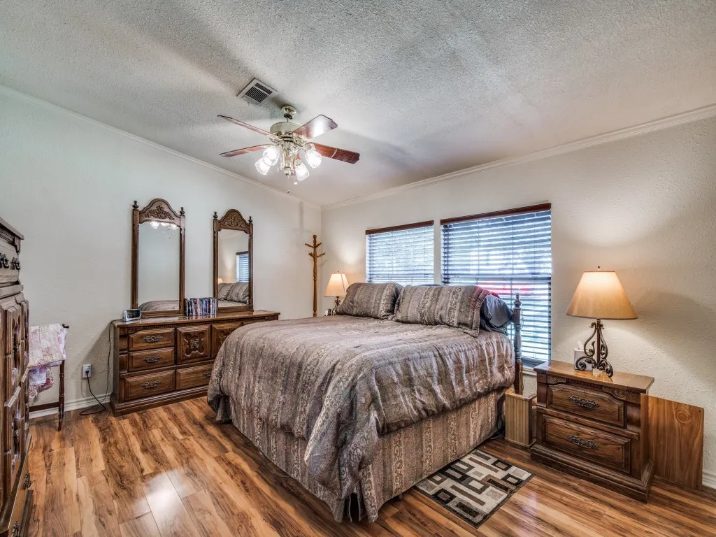Bedroom featuring wood finished floors, ornamental molding, a textured ceiling, a textured wall, and ceiling fan
