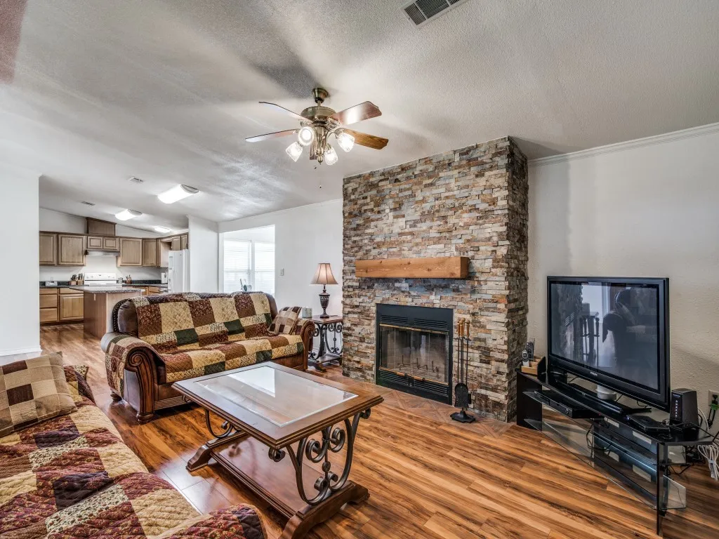 Living area with light wood-type flooring, a textured ceiling, a stone fireplace, and ceiling fan