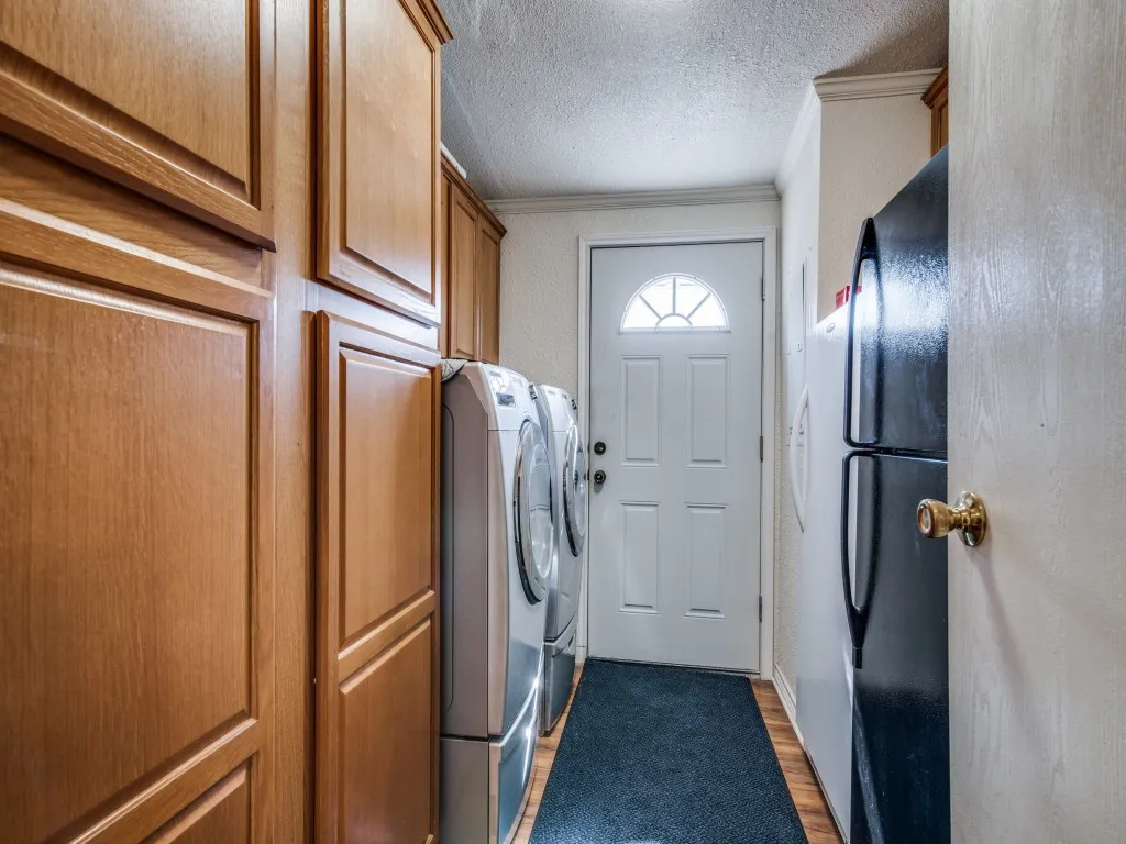 Laundry area with light wood-type flooring, a textured ceiling, washing machine and clothes dryer, crown molding, and cabinet space