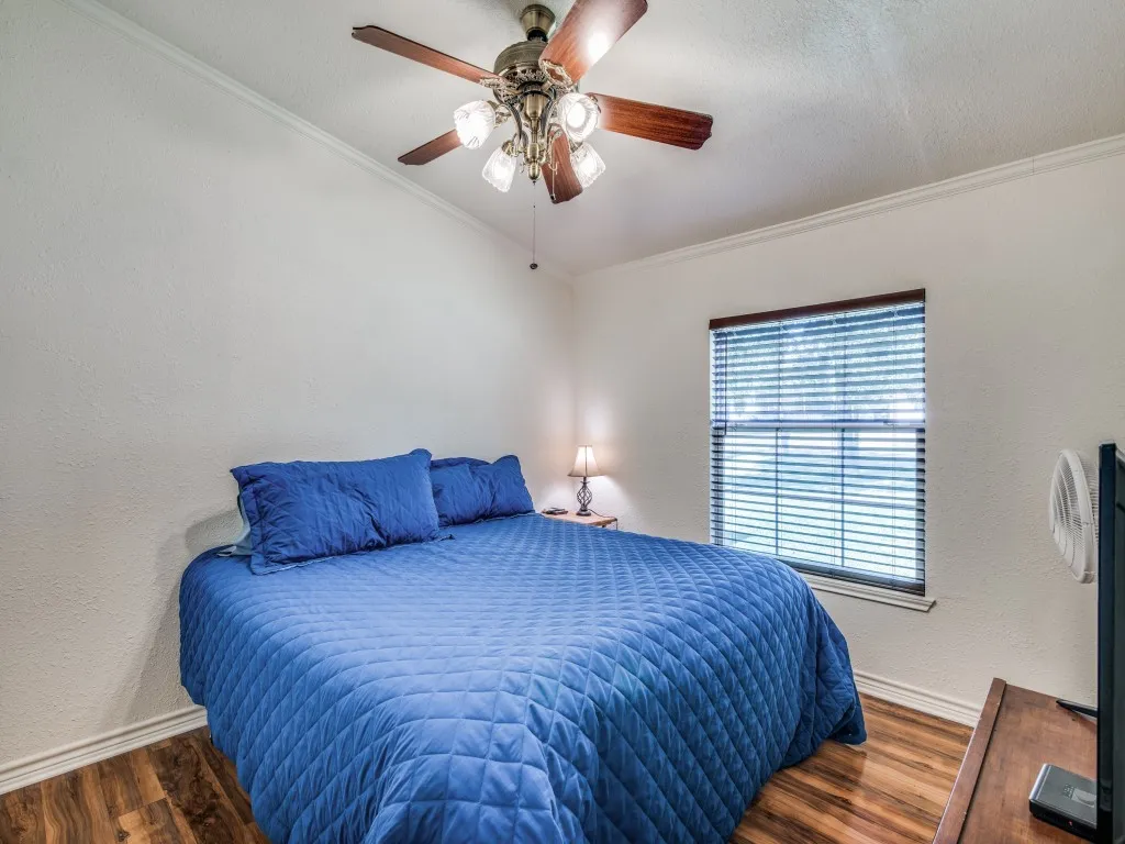 Bedroom with a textured wall, ornamental molding, wood finished floors, ceiling fan, and a textured ceiling