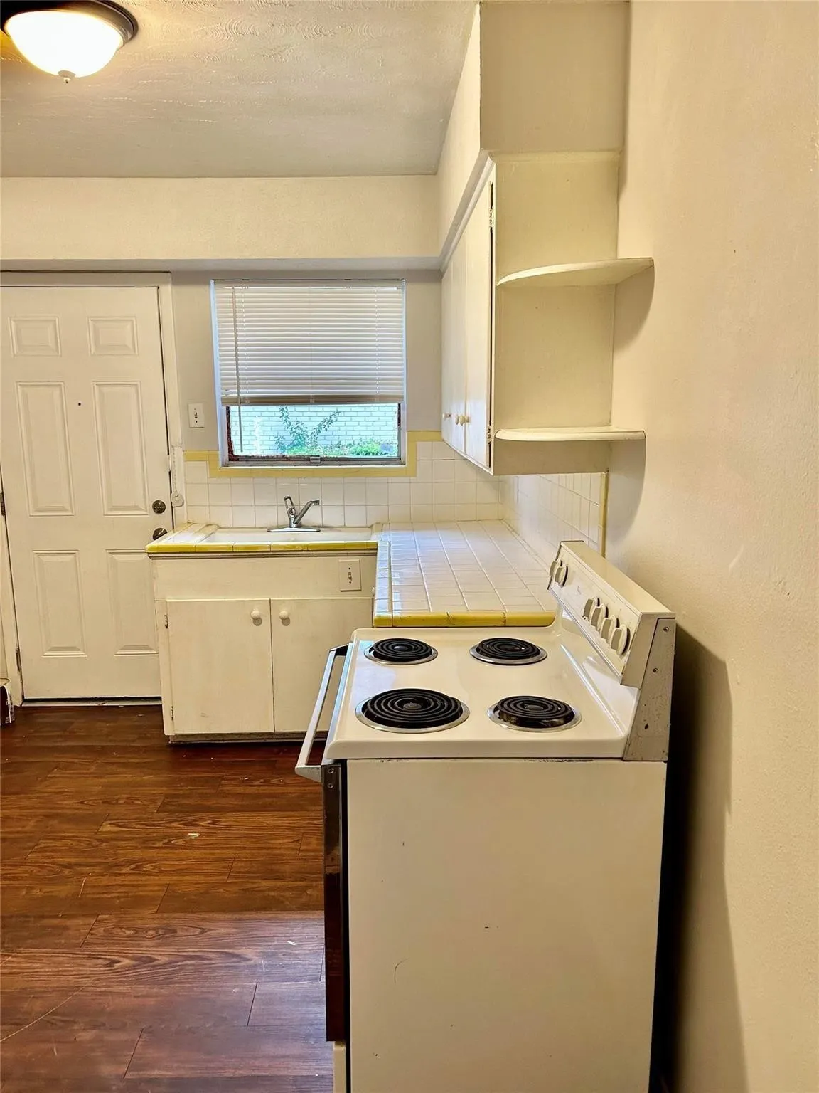 Kitchen featuring tile countertops, white electric range oven, open shelves, decorative backsplash, and dark wood-type flooring