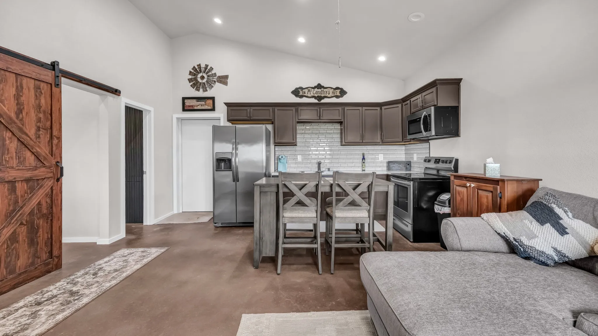 Kitchen with stainless steel appliances, backsplash, dark brown cabinetry, a barn door, and finished concrete flooring