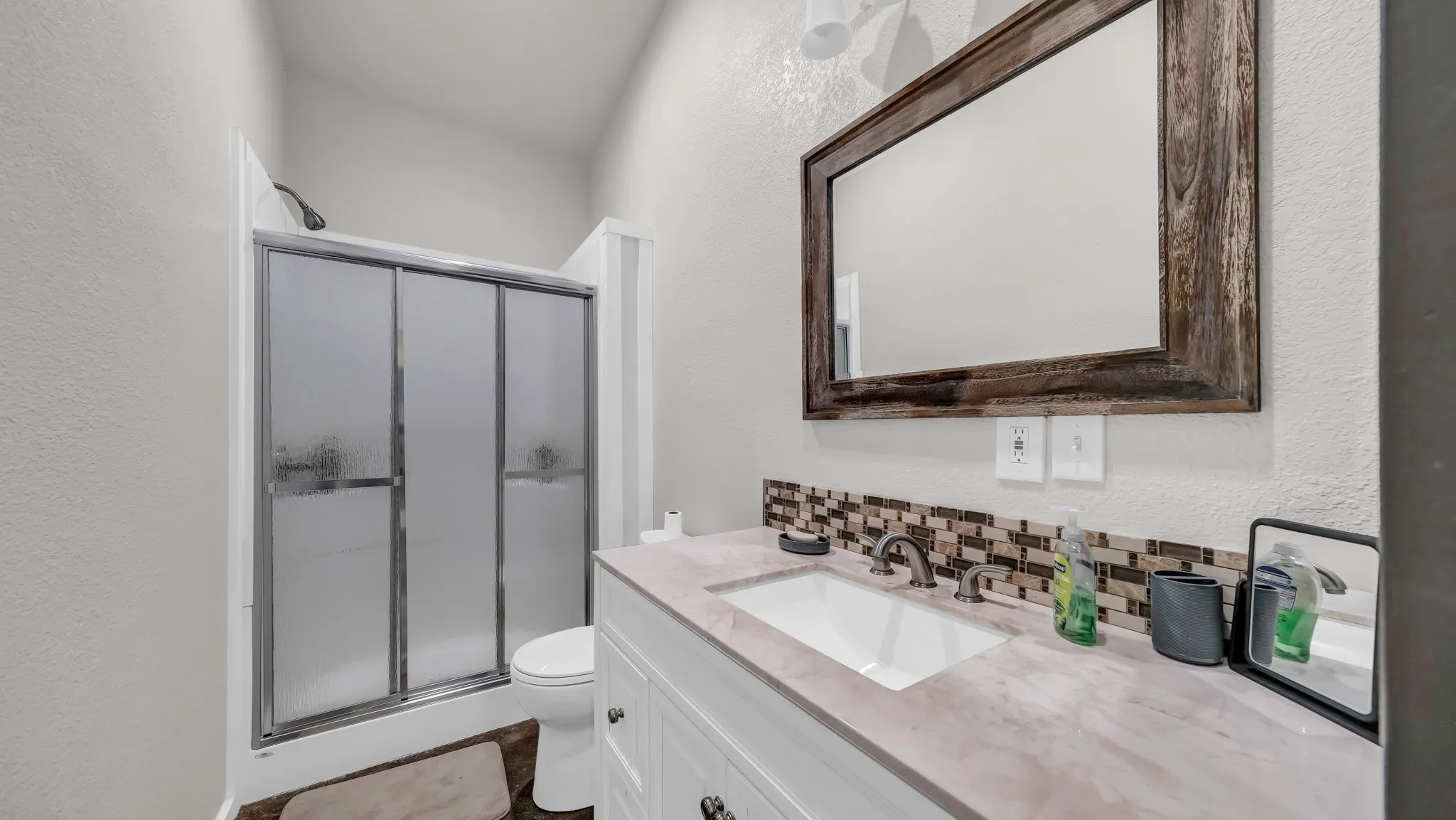 Full bath with a textured wall, a shower stall, decorative backsplash, and vanity